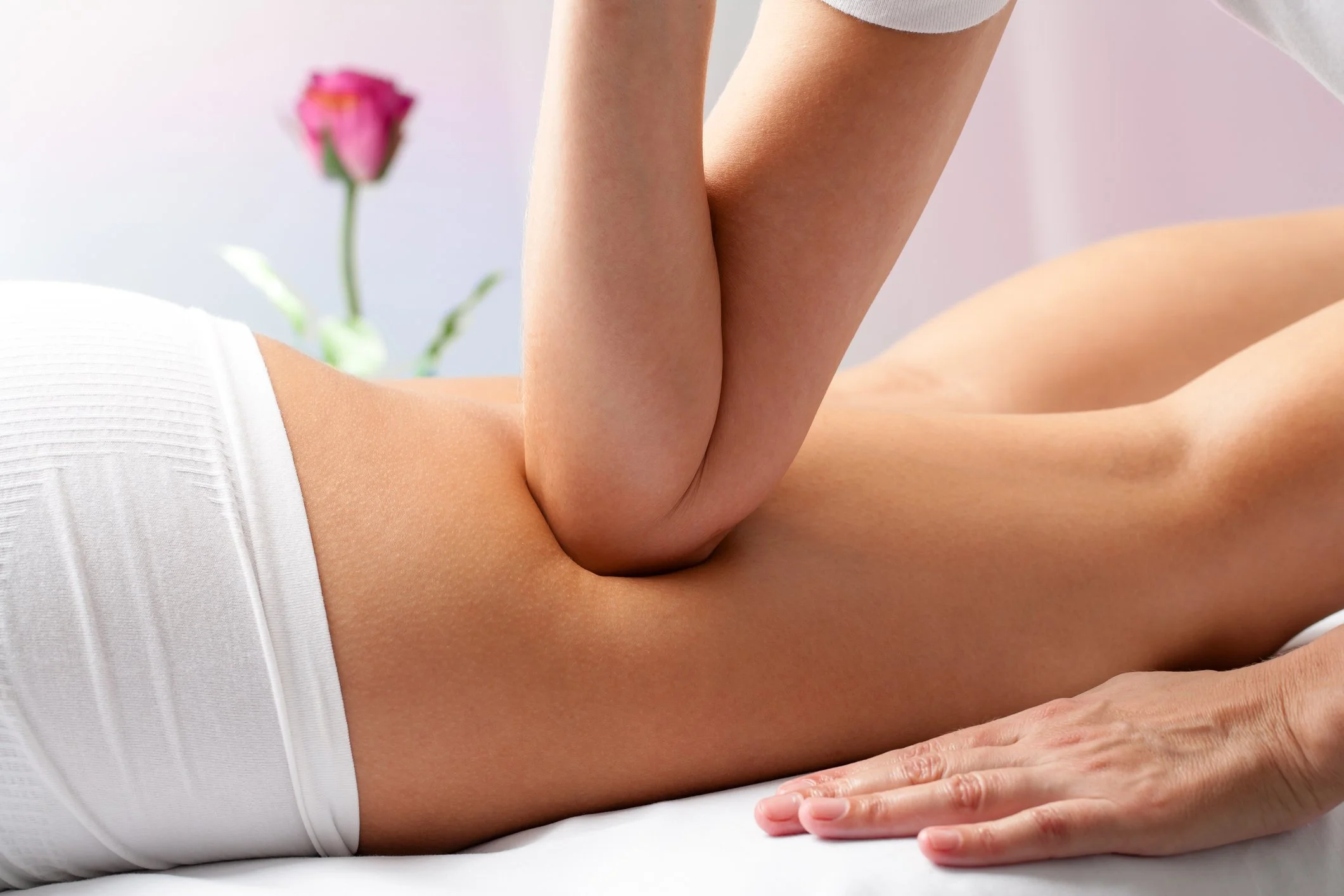 Close-up of a person receiving a massage, lying face down on a massage table, with a pink flower in the background.