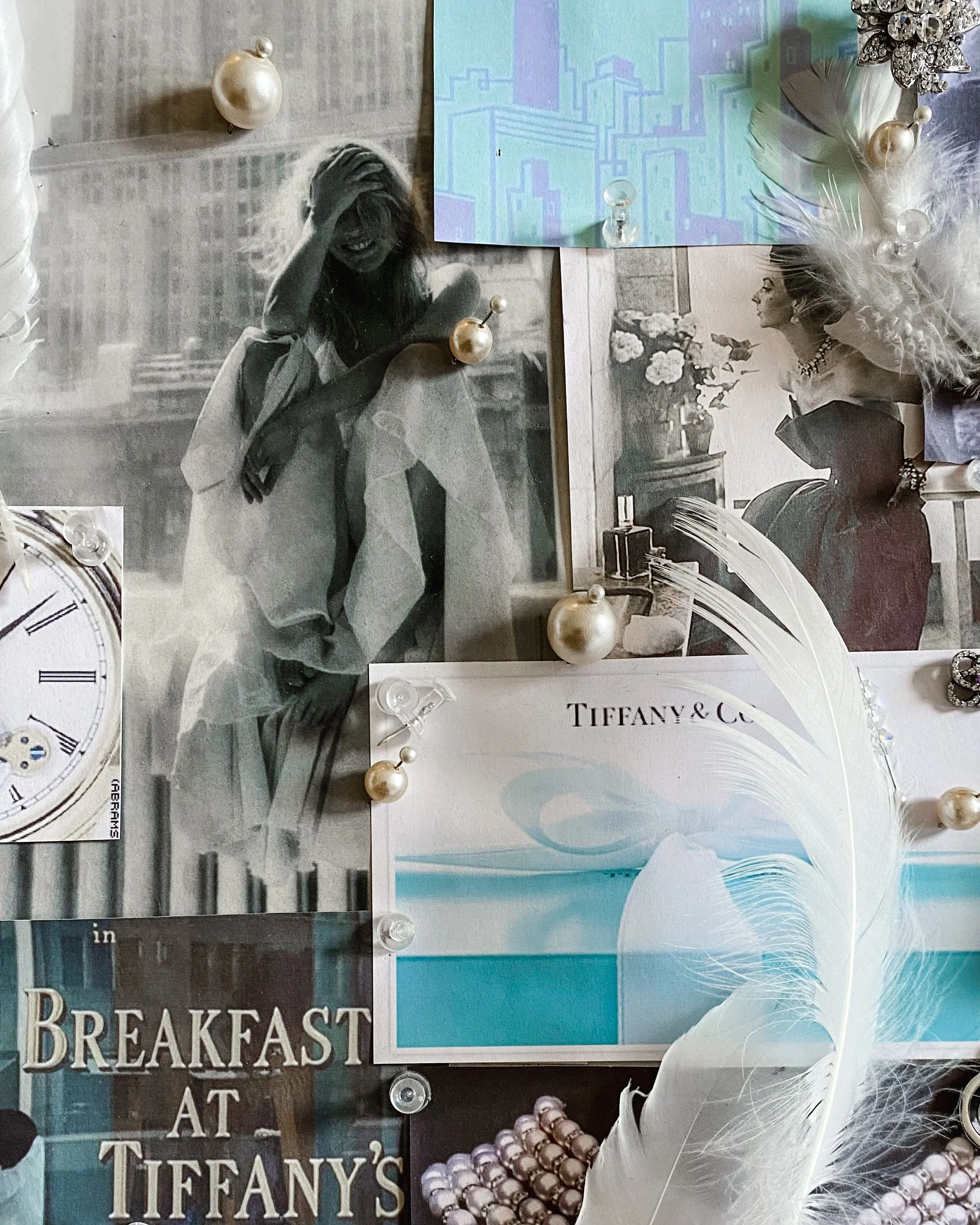 A close up photo of the mood board, with images, a white feather and pinned pearl beads.