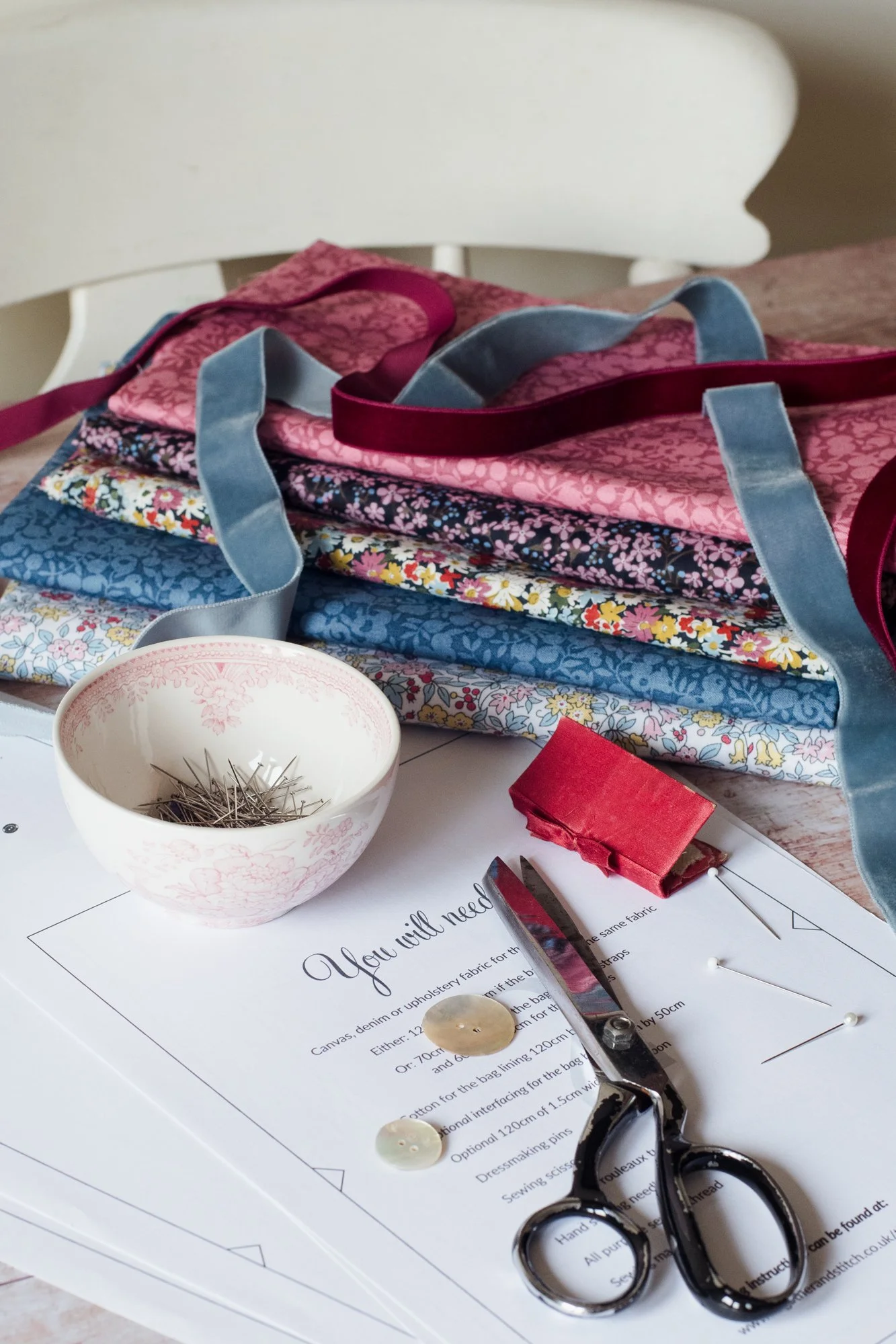 Folded Liberty fabrics and a To Gather And Stitch sewing pattern and dressmaking scissors on a  wooden tabletop