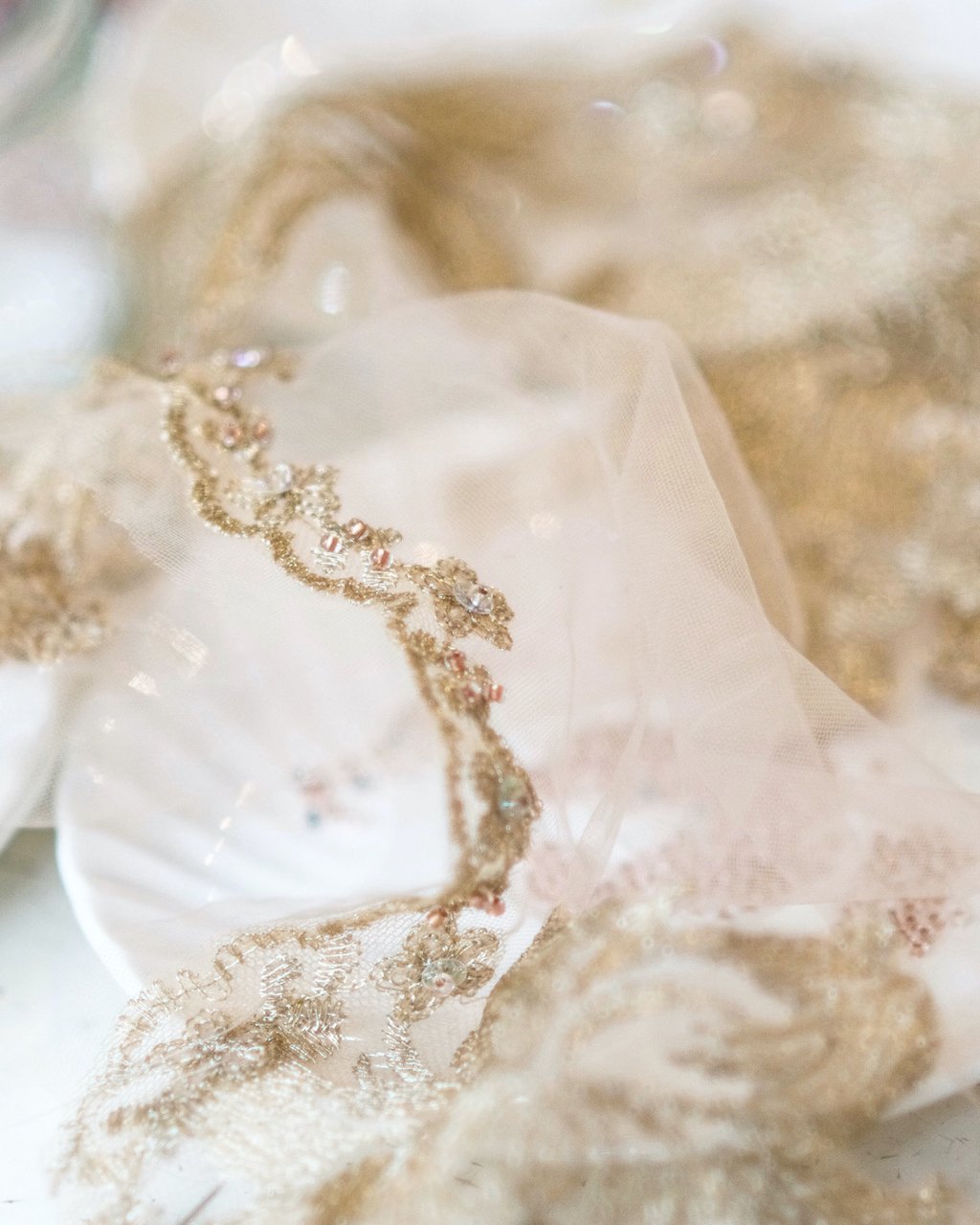 A close up photograph of work in progress on the sewing table in the atelier, showing a saucer with vintage glass beads and a hand beaded edge of a tulle and lace cape.
