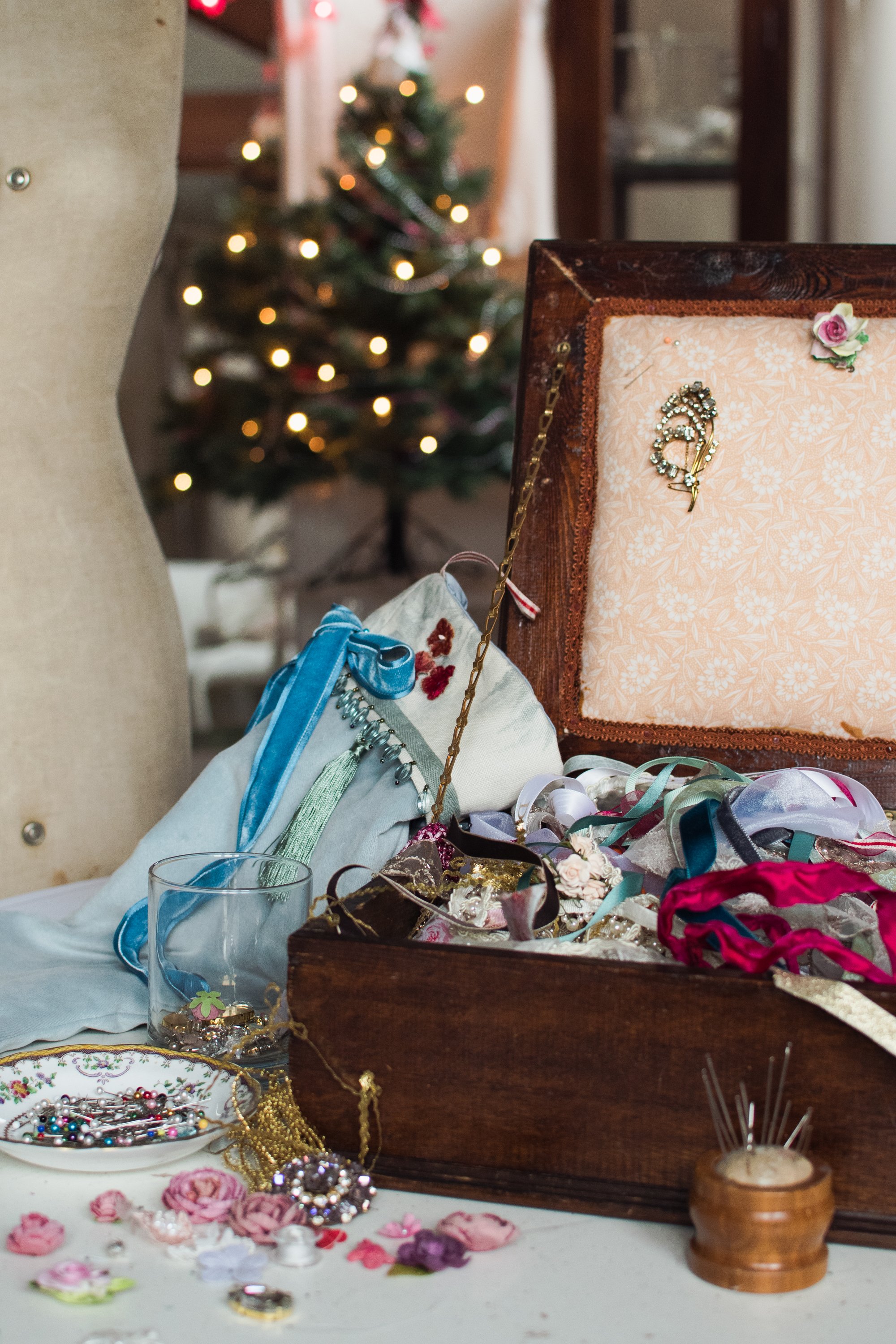 A view of the studio during a Christmas Stocking workshop, with a stocking in blue velvet, a wooden workbox  ona  table fille with ribbons and trims , and in the background a mannequin and a Christmas tree