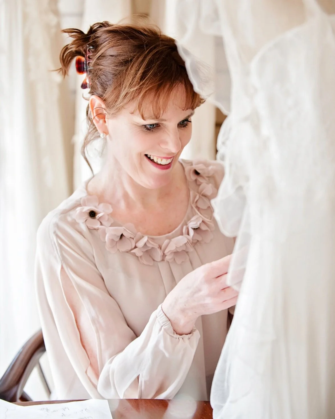 A photograph of Sarah working in her design studio surrounded by couture lace dresses.