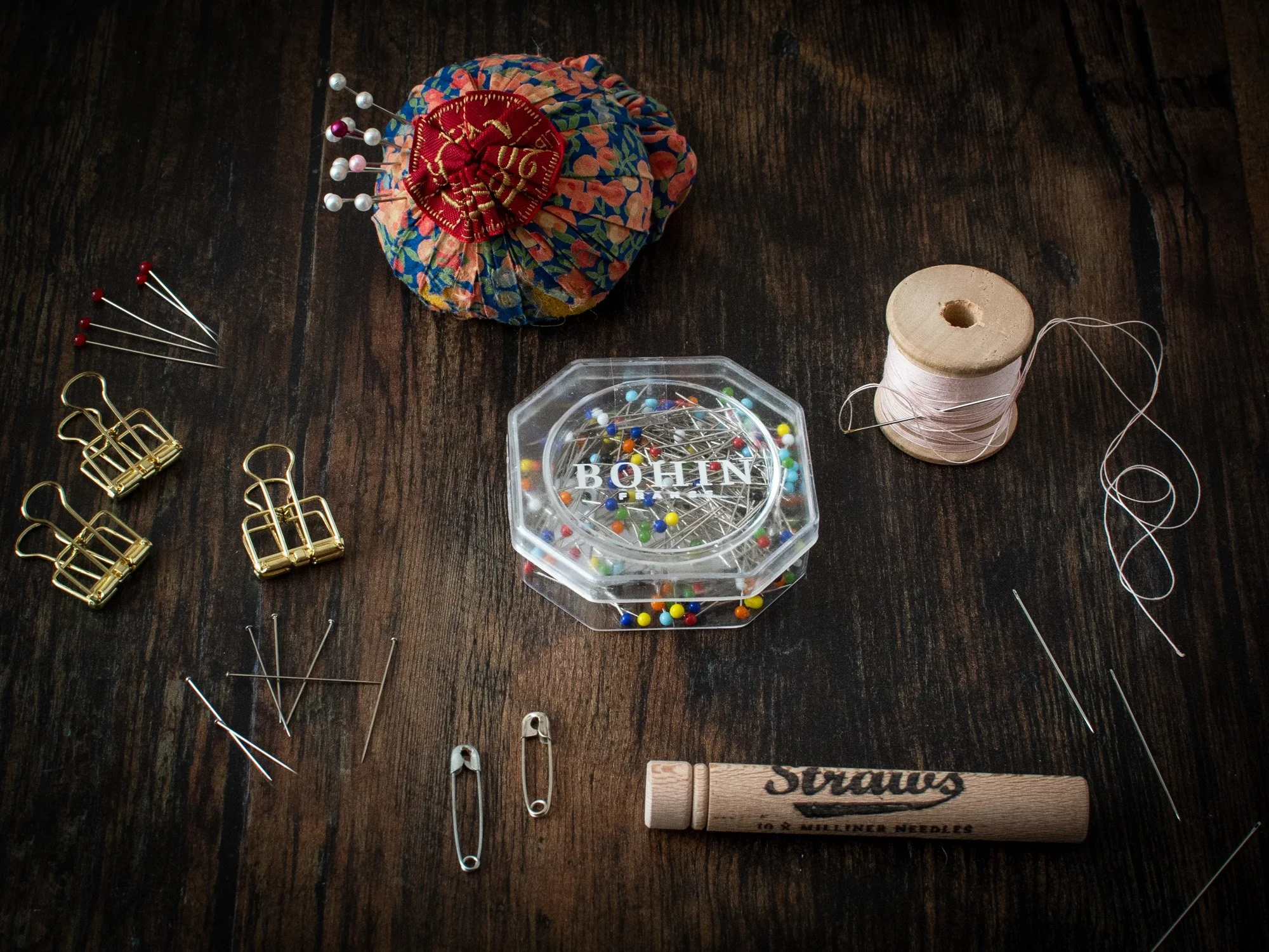 A flay lay display of dressmaking pins and hand sewing needles on a dark wooden tabletop