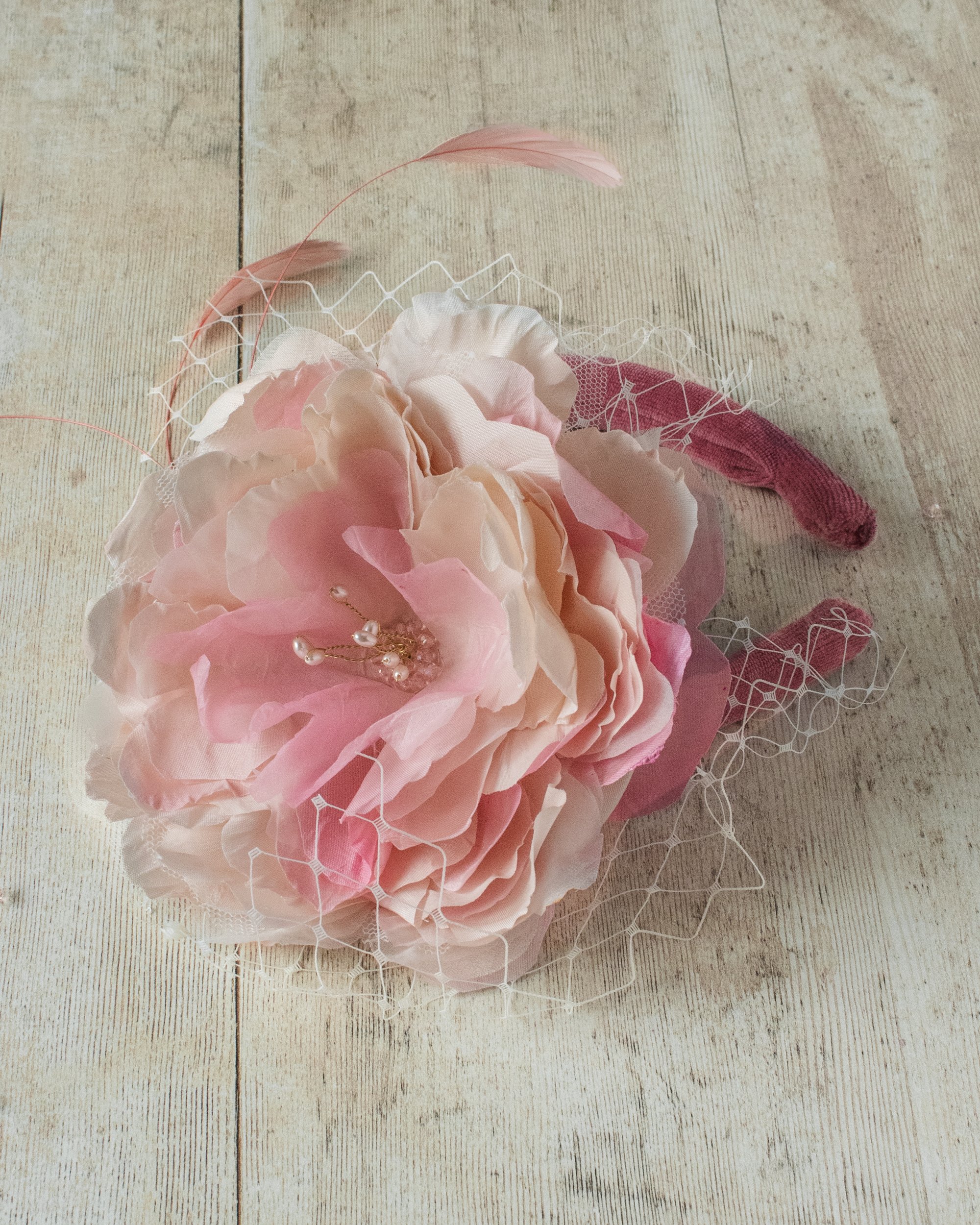 A pink floral hair accessory with a pearl and gold embellishment, placed on a light wooden surface.