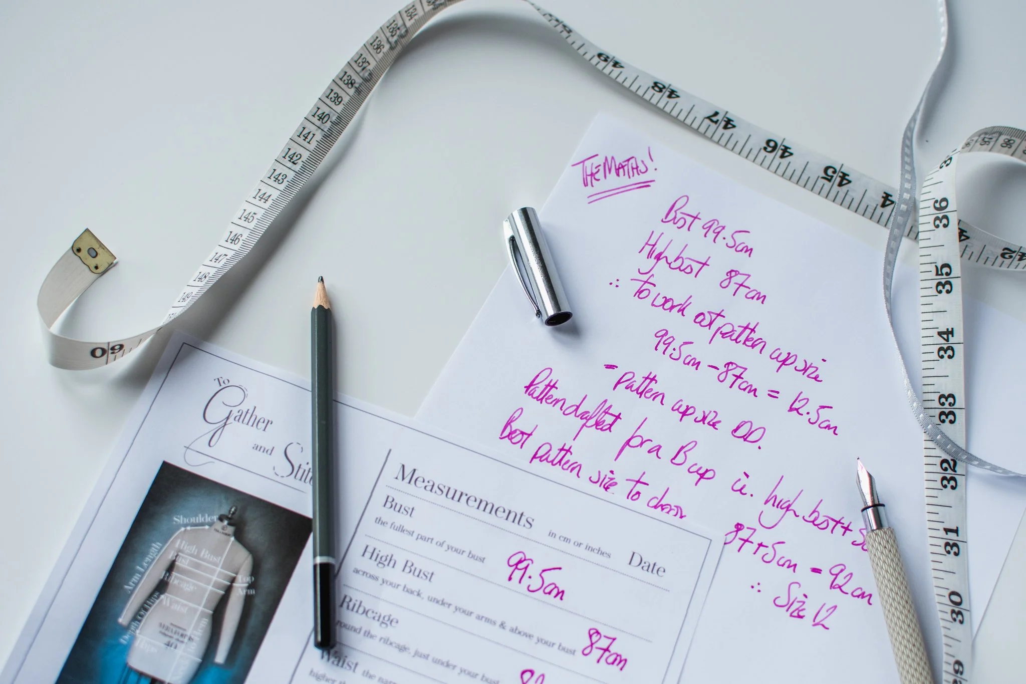 A measurement chart, pen and tape measure, and working out the maths for a  full bust adjustment on a piece of paper.