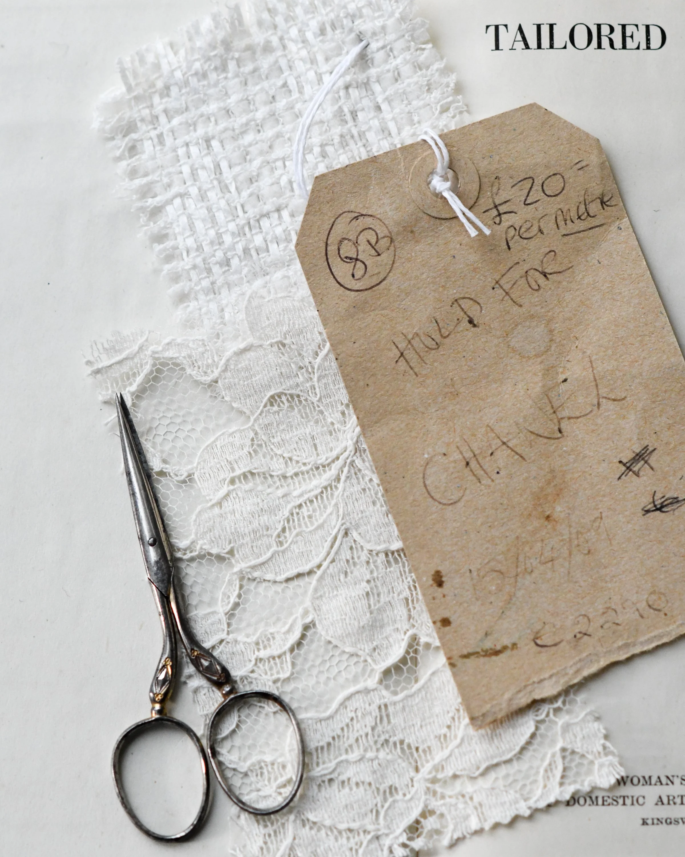 A brown manilla label saying "Hold for Chanel" , Chanel Tweed and cotton lace fabric.