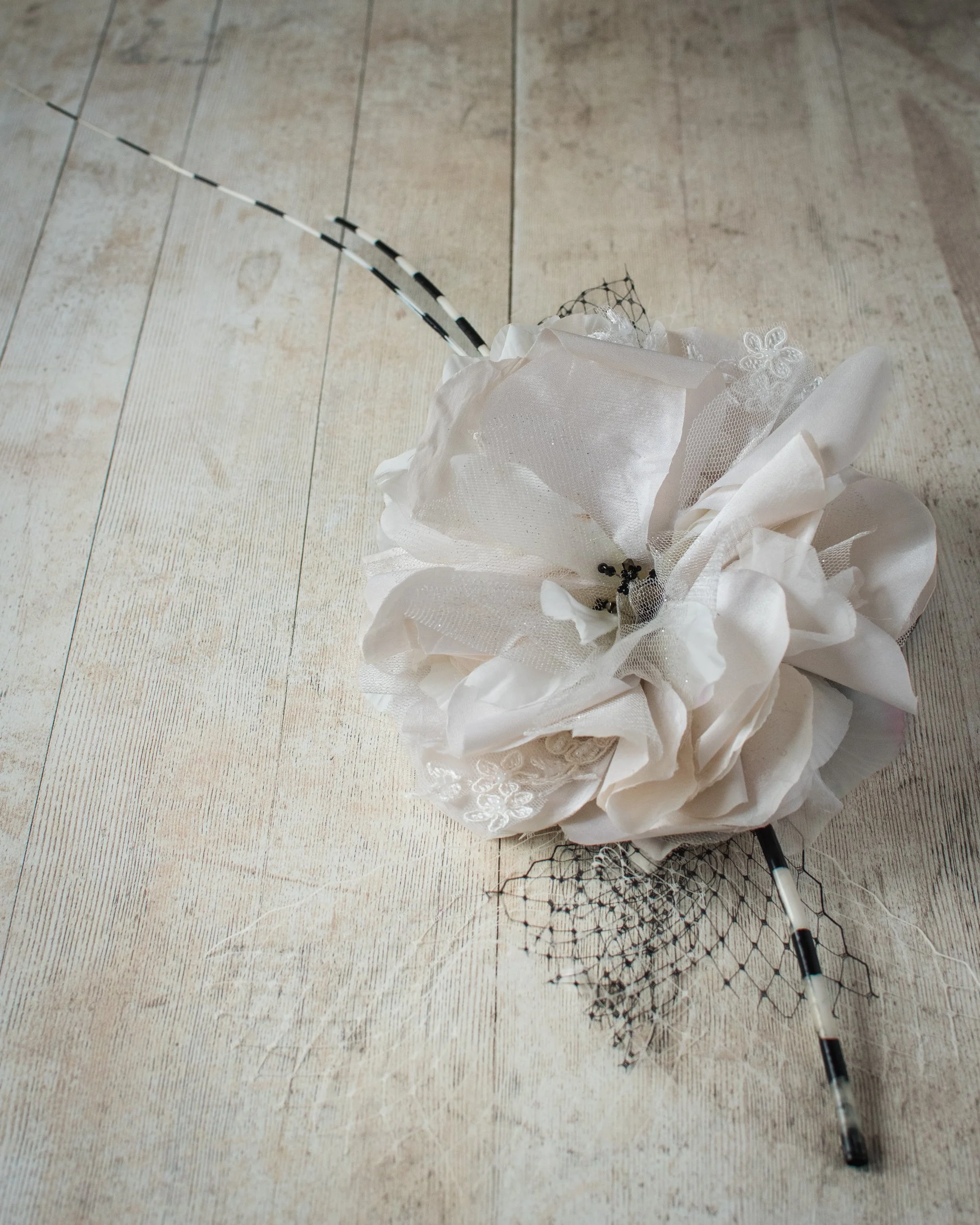 A white decorative flower with black and white striped antennae and a net-like structure at the base is lying on a wooden floor.