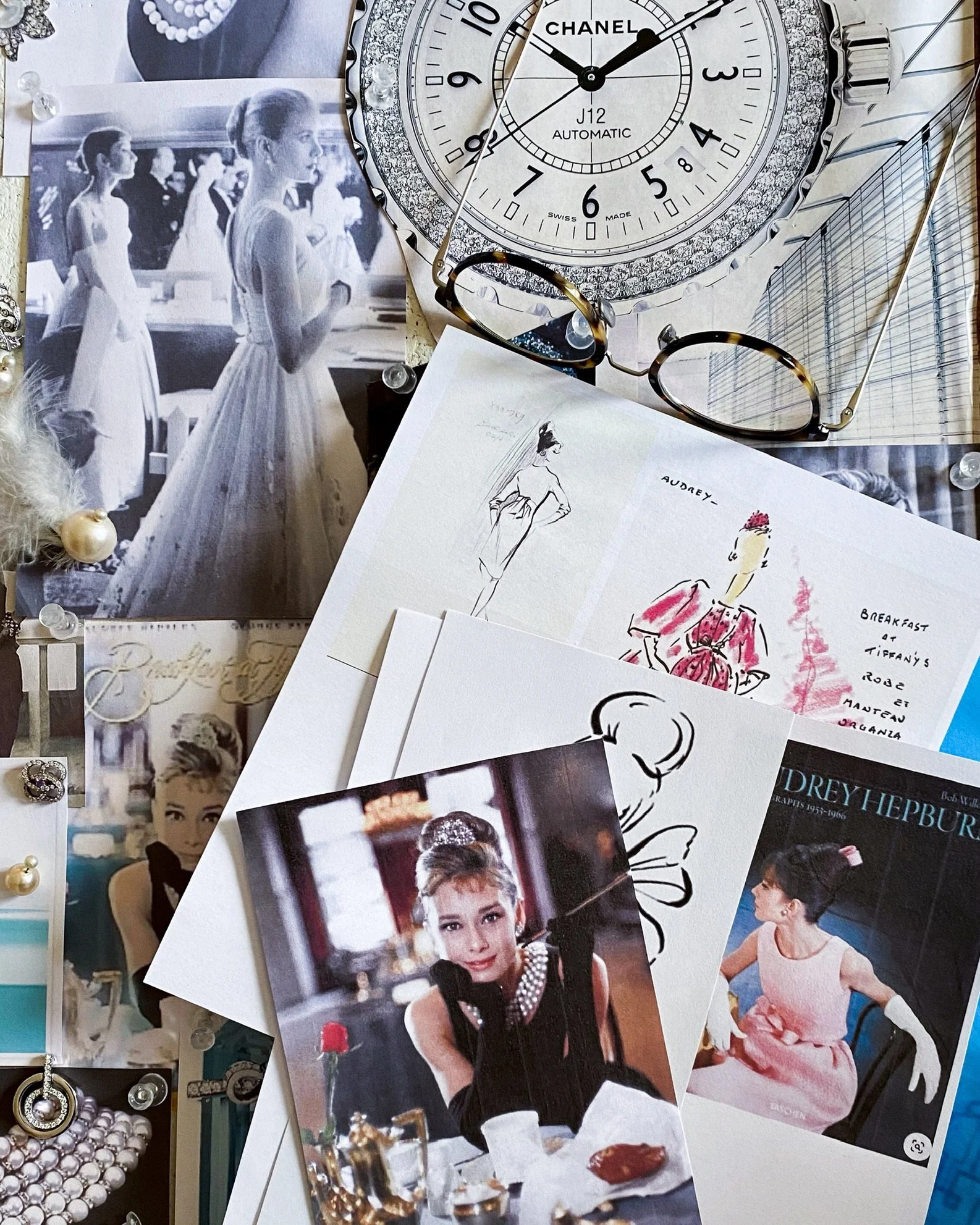 A messy pile of inspiring images and magazine cuttings for an inspiration board, on a  tabletop with a pair of glasses