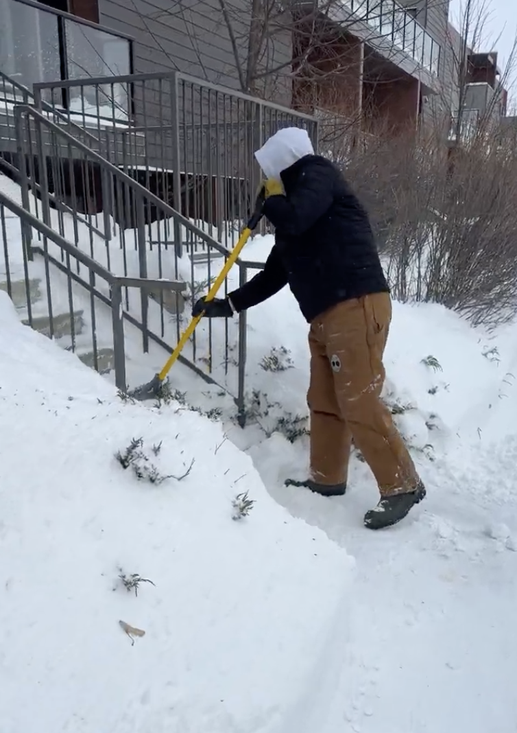 A person shoveling snow off stairs outside a building during winter.