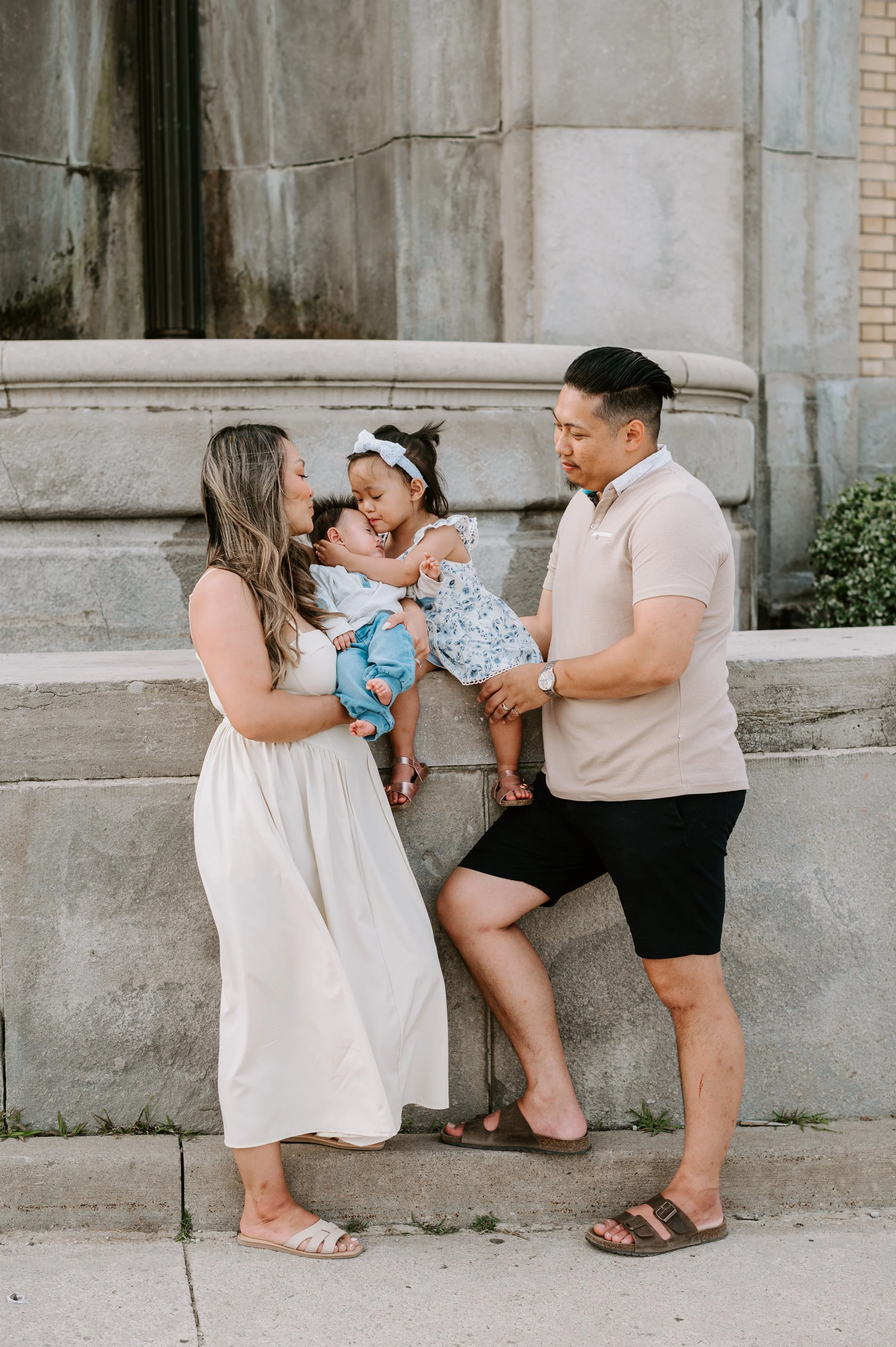 mother and father with their two children outside. The daughter who is 2.5 years old is hugging her baby brother. GTA family photography, Toronto family photography, family photographer