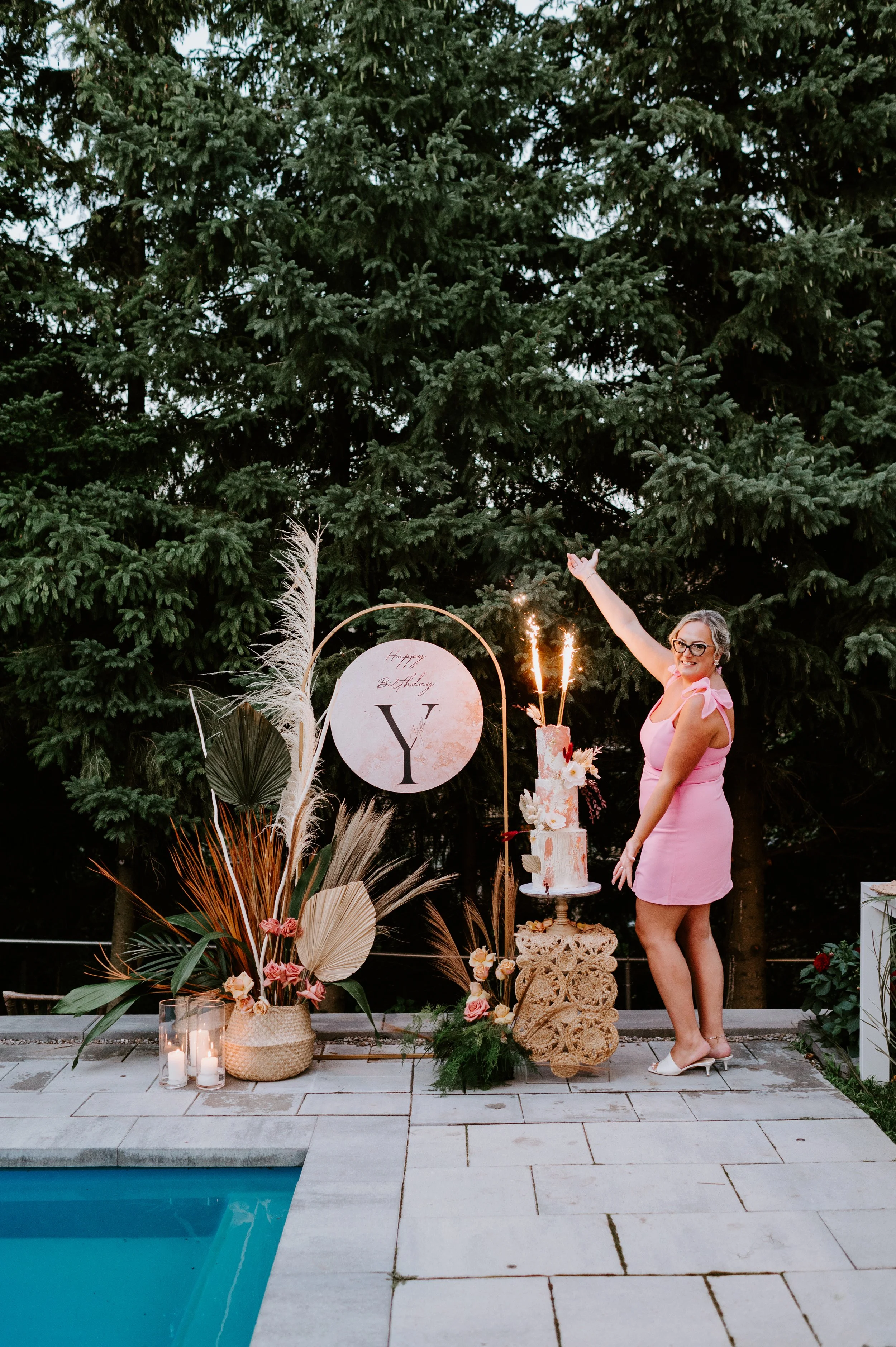 a woman celebrating her birthday. She is holding sparklers and is standing beside her cake outside during her backyard party. Milestone photography, toronto milestone photography