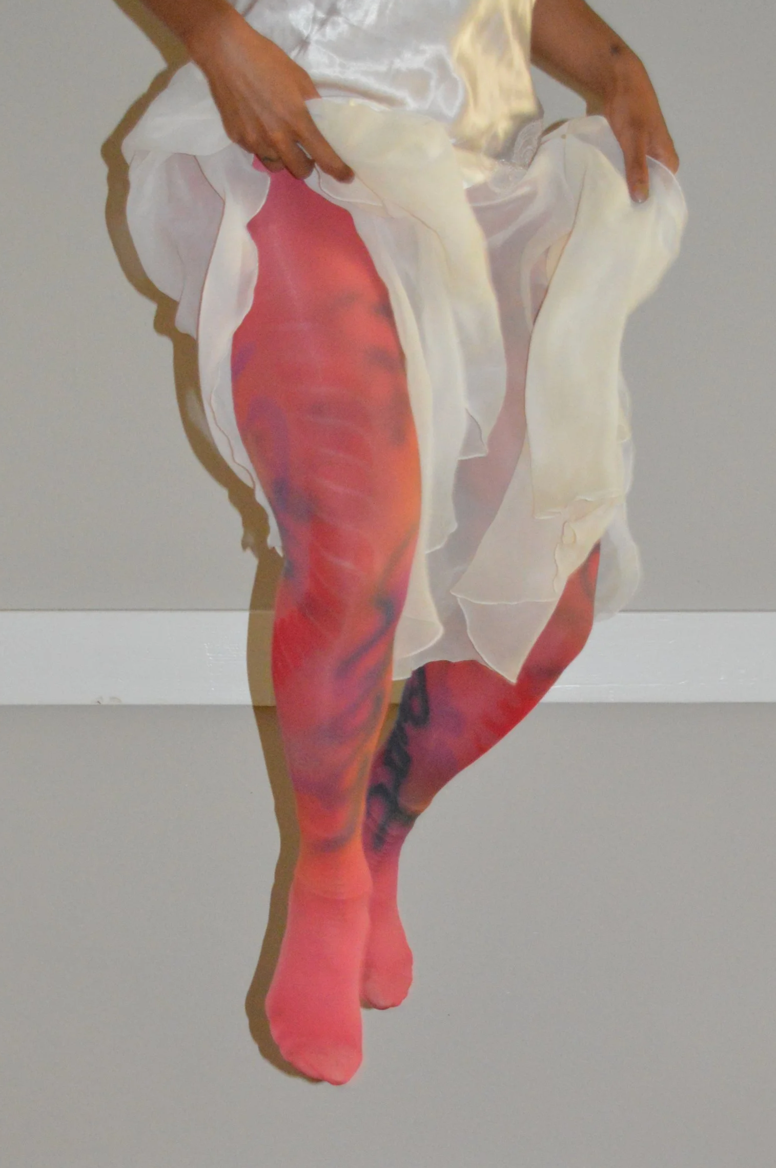 Close-up of a person lifting a sheer white garment to reveal colorful, patterned tights.