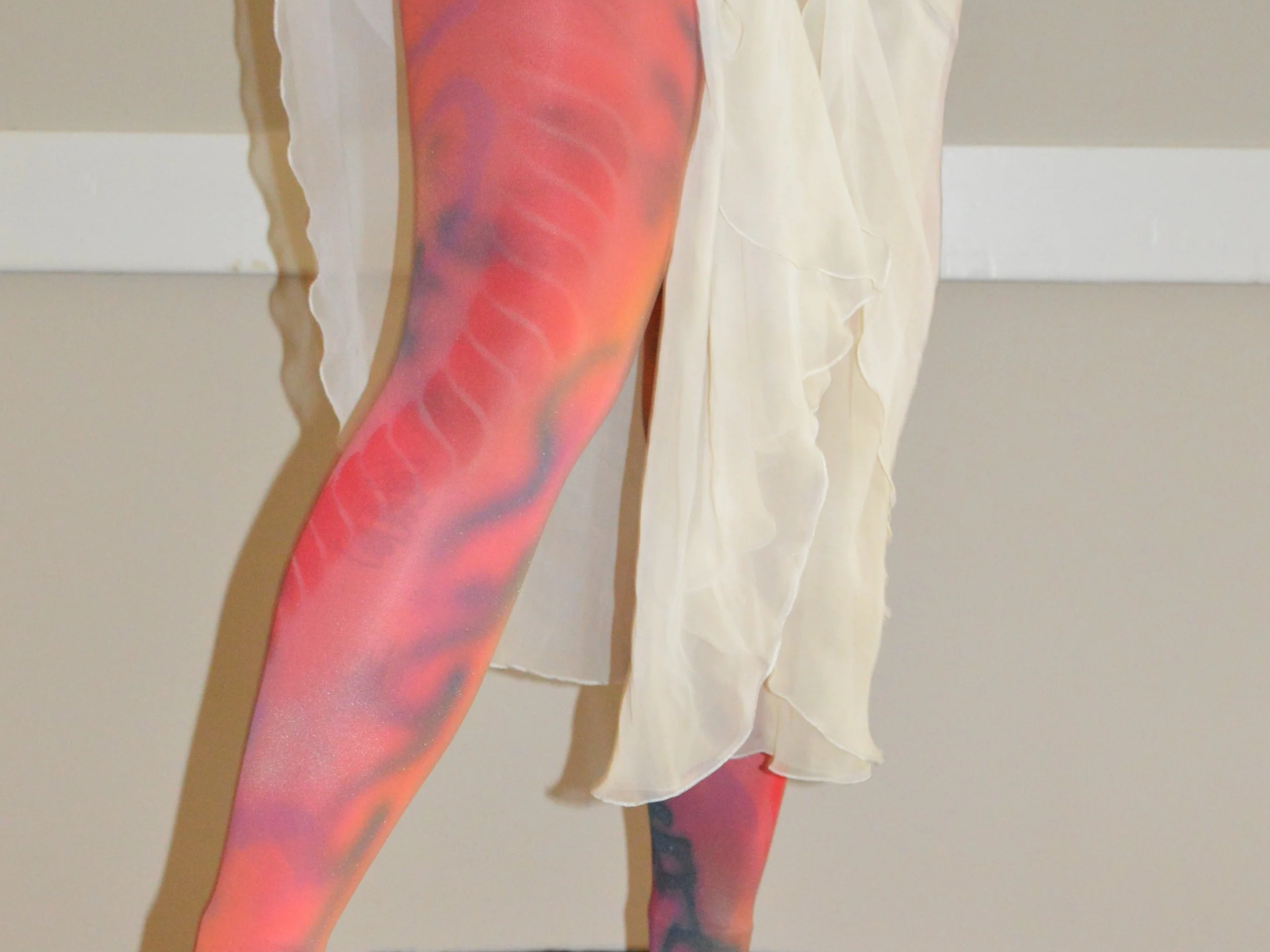 Close-up of a leg with colorful, abstract body paint, wearing a flowing, cream-colored dress.