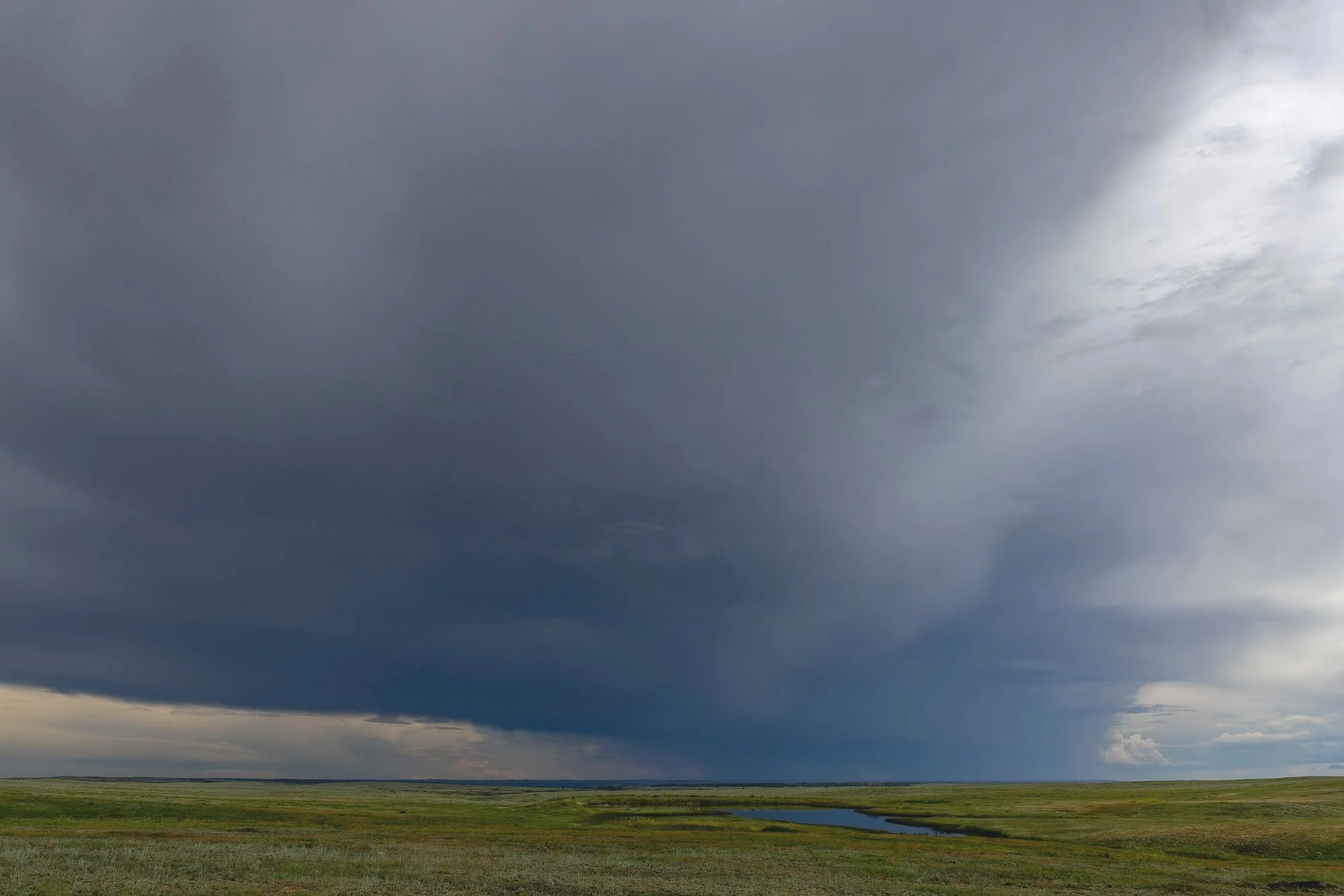 Dark storm clouds over an open grassy plain with a small river or creek in the distance.