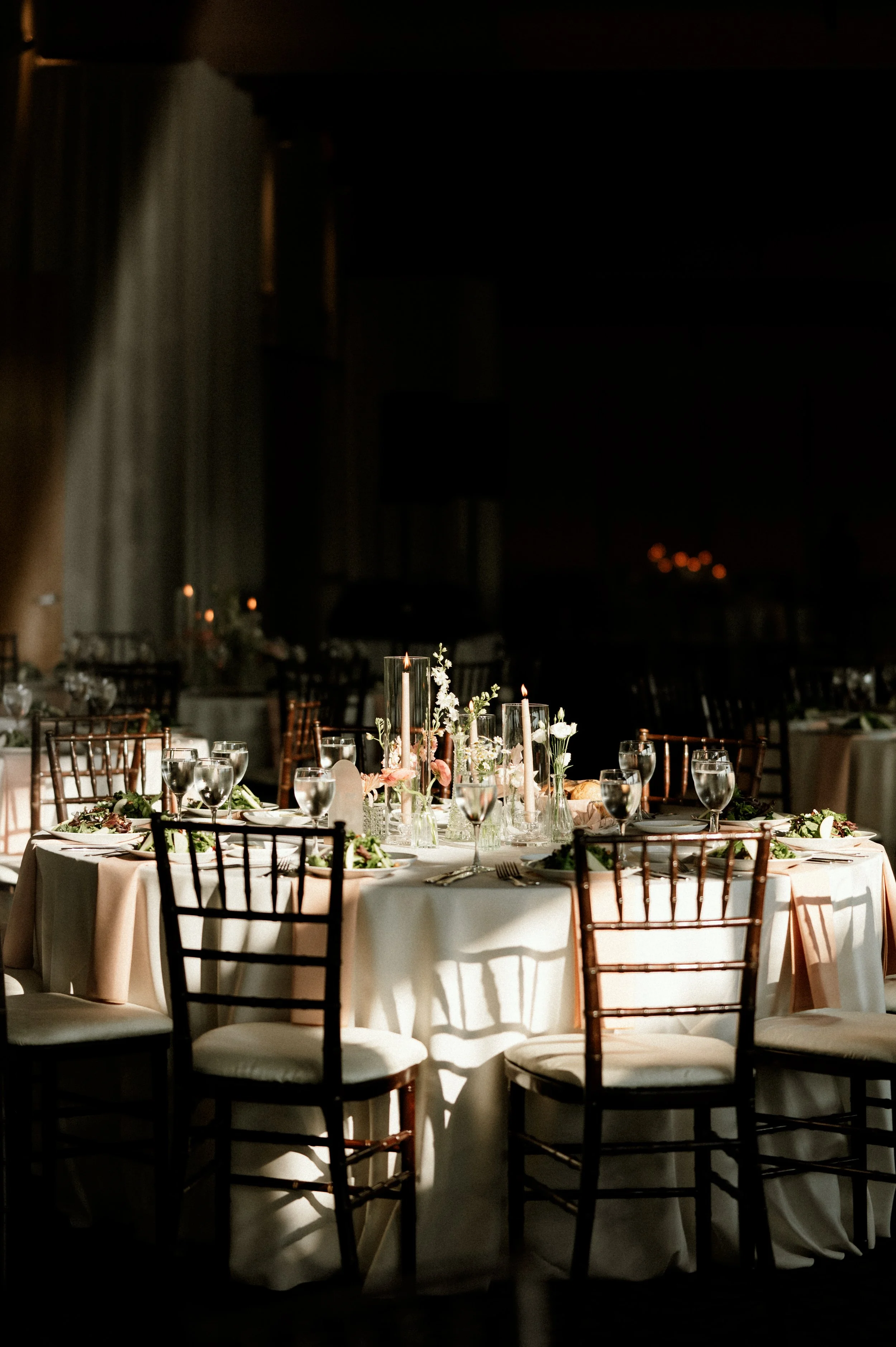 Elegant wedding reception table with floral centerpieces and candles in a dimly lit room.