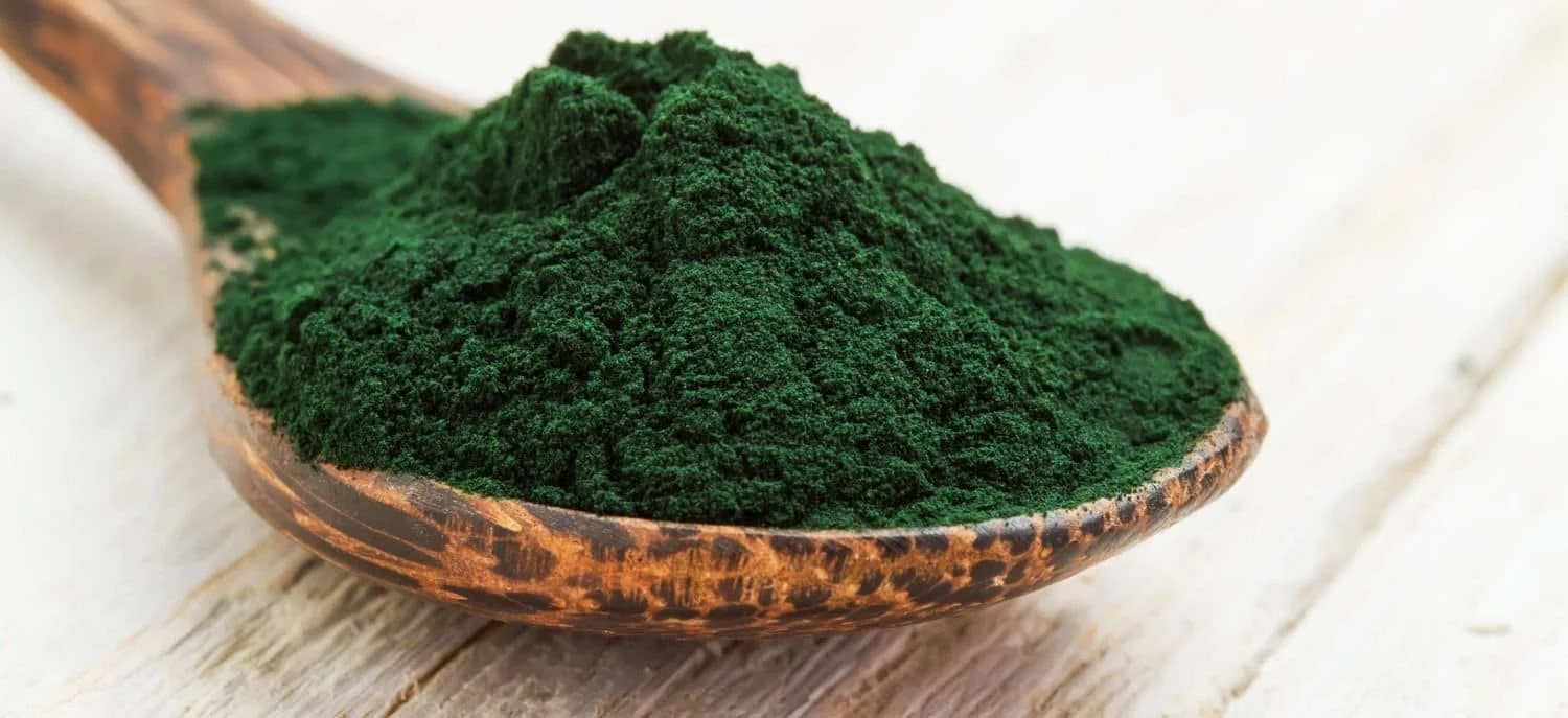 A wooden spoon overflows with vibrant green powder, resting on a white wooden surface.