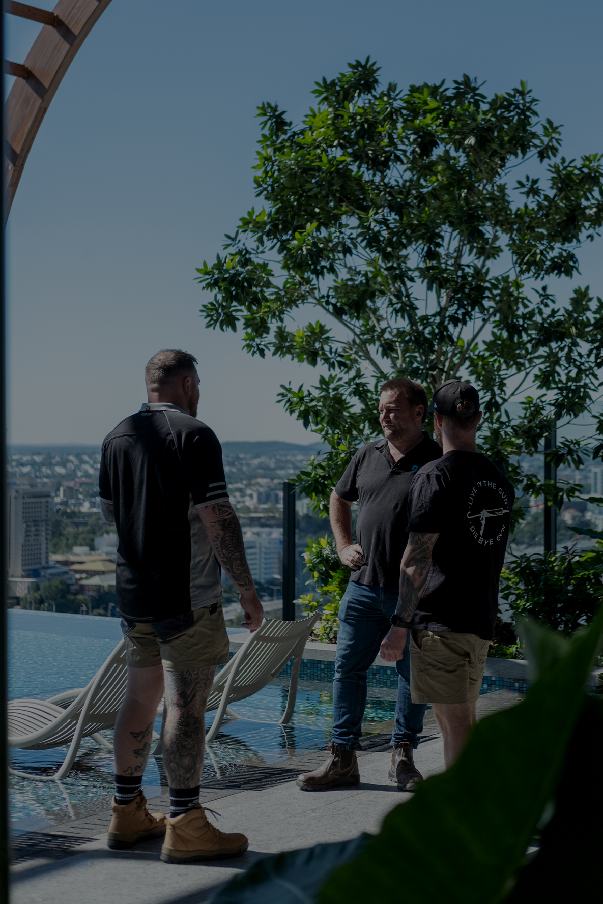 Three men standing near a rooftop pool with a city view.