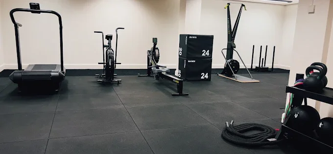 Cardio corner with equipment, plyometric boxes, battle ropes, kettlebells, and medicine balls on a black rubber floor