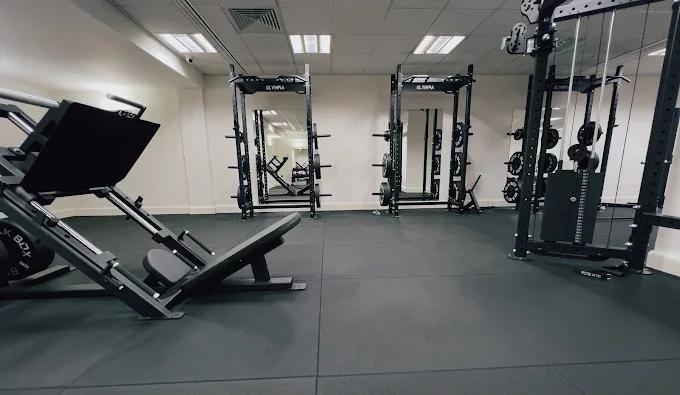 Esclusive gym with weightlifting equipment, including a leg press machine on the left and power racks in the background.