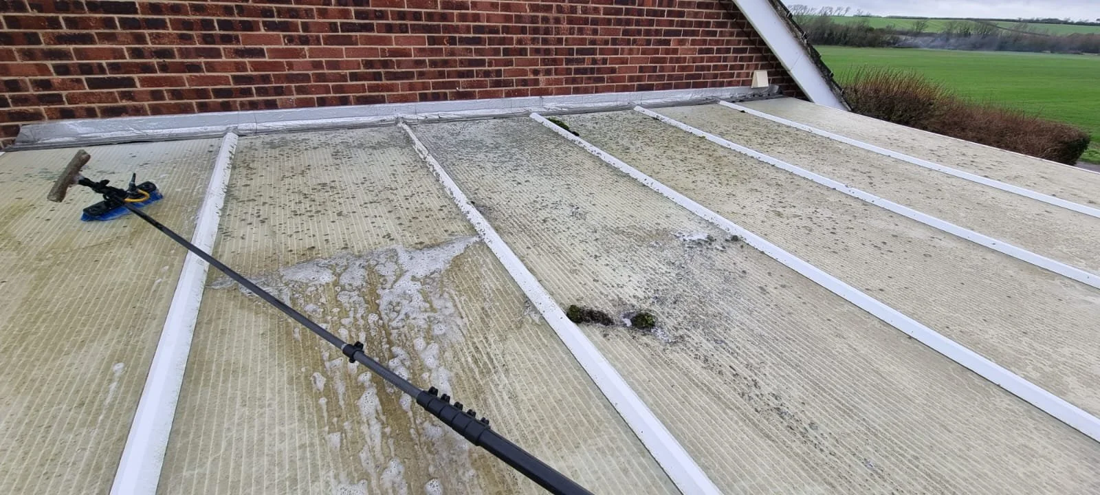 View of a Perspex conservatory roof during cleaning, revealing clean and dirty sections of the surface.