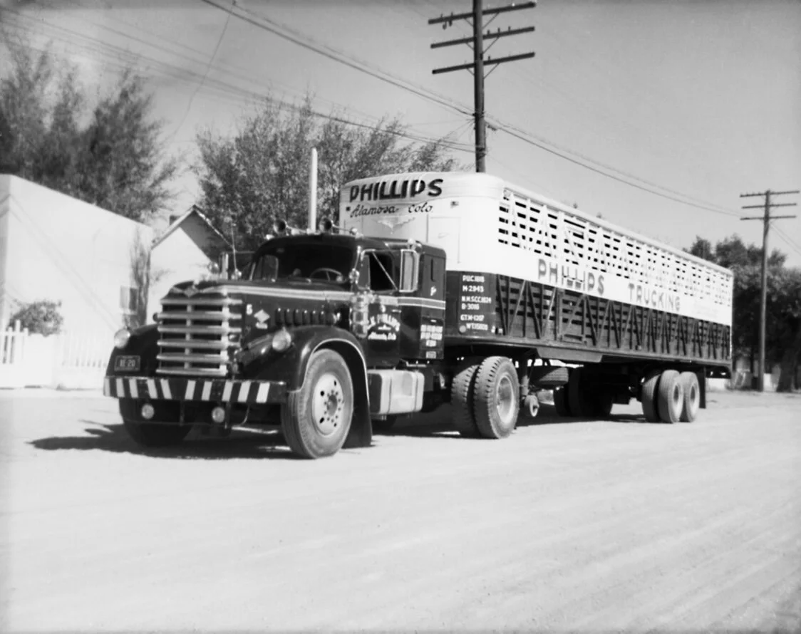 Black and white image of a vintage semi-truck that has the name "Phillips" on the trailer of the truck.