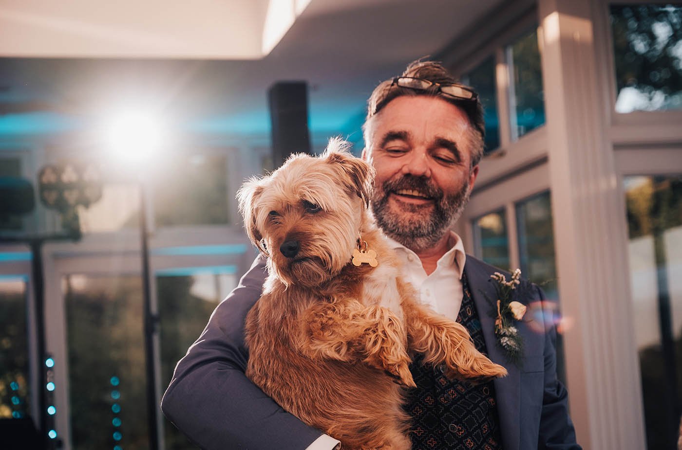 A heartwarming moment captured as the groom lovingly carries his furry best friend, perhaps taking a moment to share the joy of the wedding day with his beloved dog.