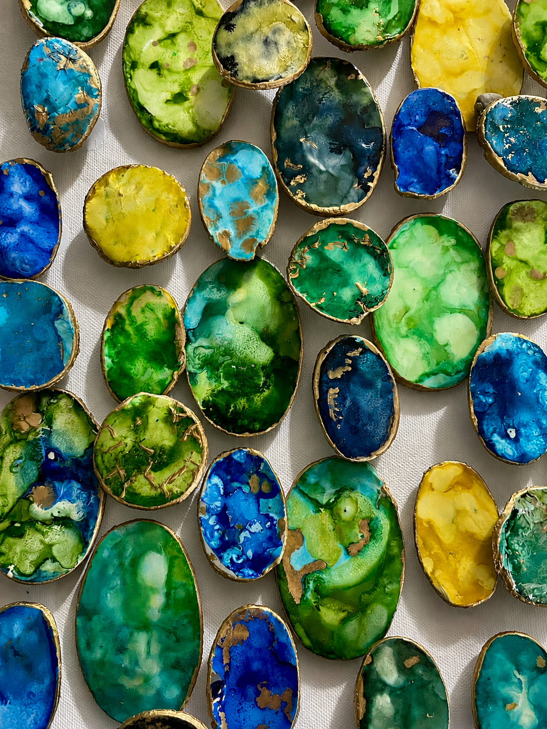 "Tide Pools" offers an intimate look at the intricate beauty of organic forms. Hand-finished dimensional pieces reveal swirling layers of vibrant greens, blues, and turquoise, accented with delicate touches of gold. Rich texture, subtle shadows, and 