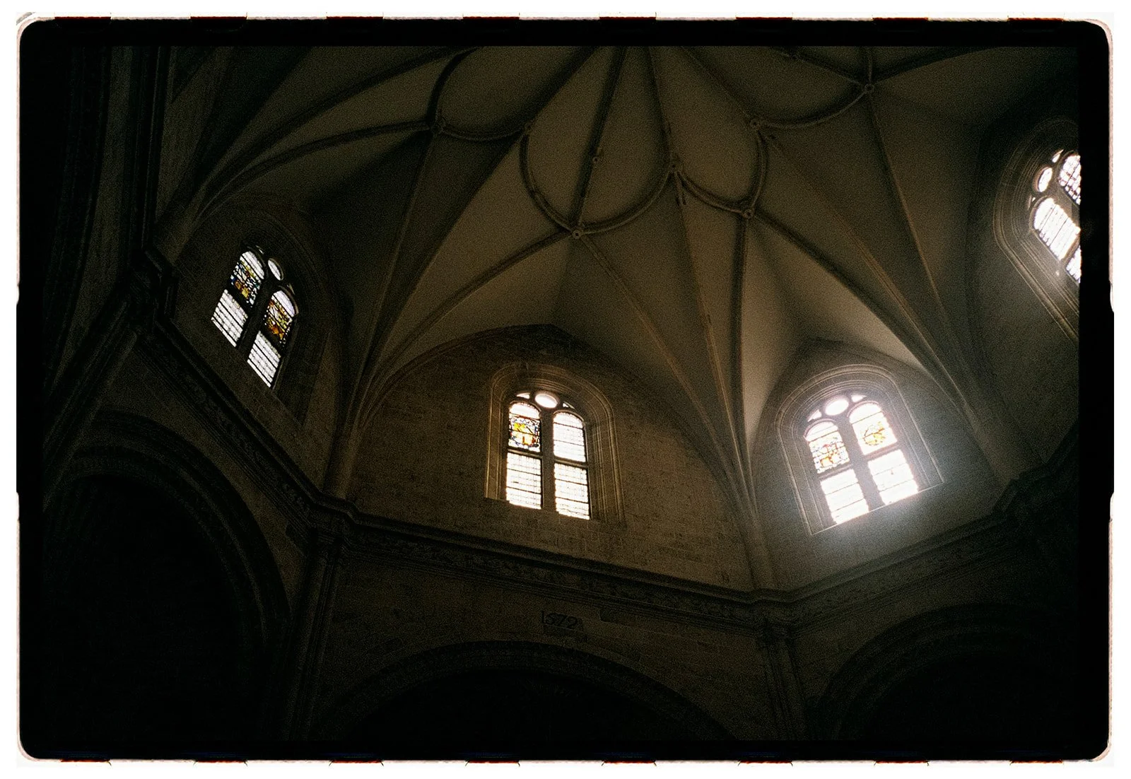 Interior view of a church ceiling with stained glass windows, vaulted arches, and detailed architecture.