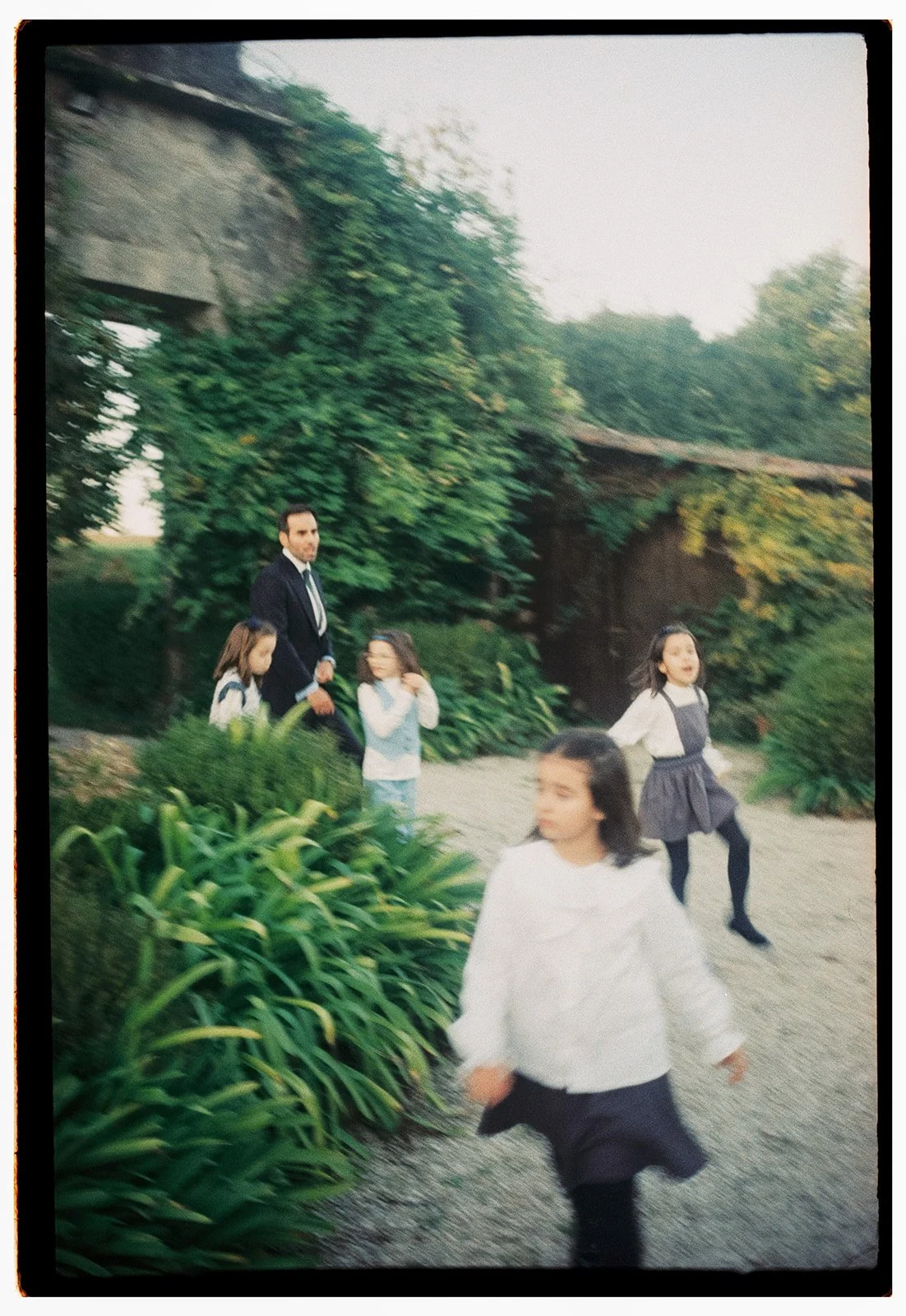 A man in a suit with four children outdoors in a garden with lush greenery and trees.