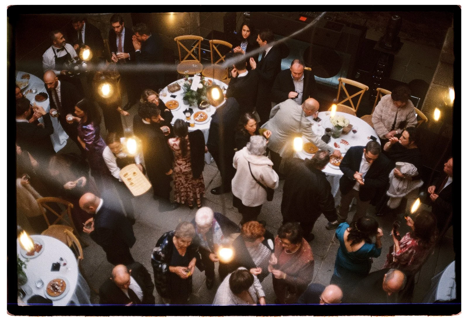 People socializing at a dinner party with round tables, food, and dim lighting.