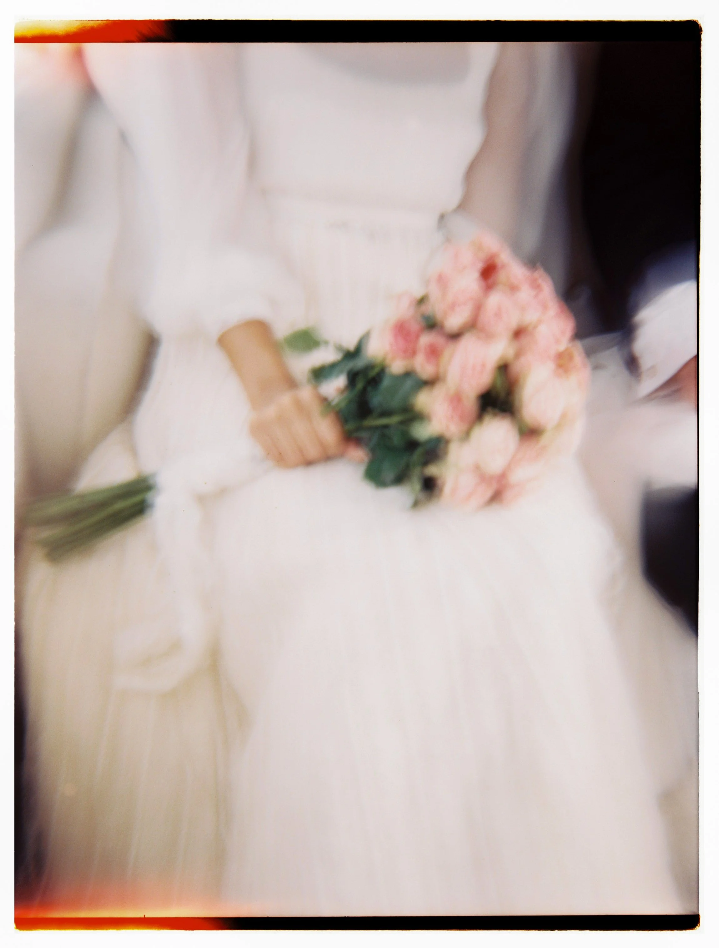 Person in white dress holding a bouquet of pink roses.