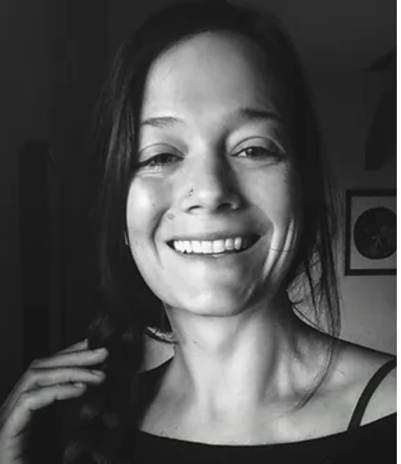 Black and white close-up of a woman with long hair smiling at the camera, wearing a black top.