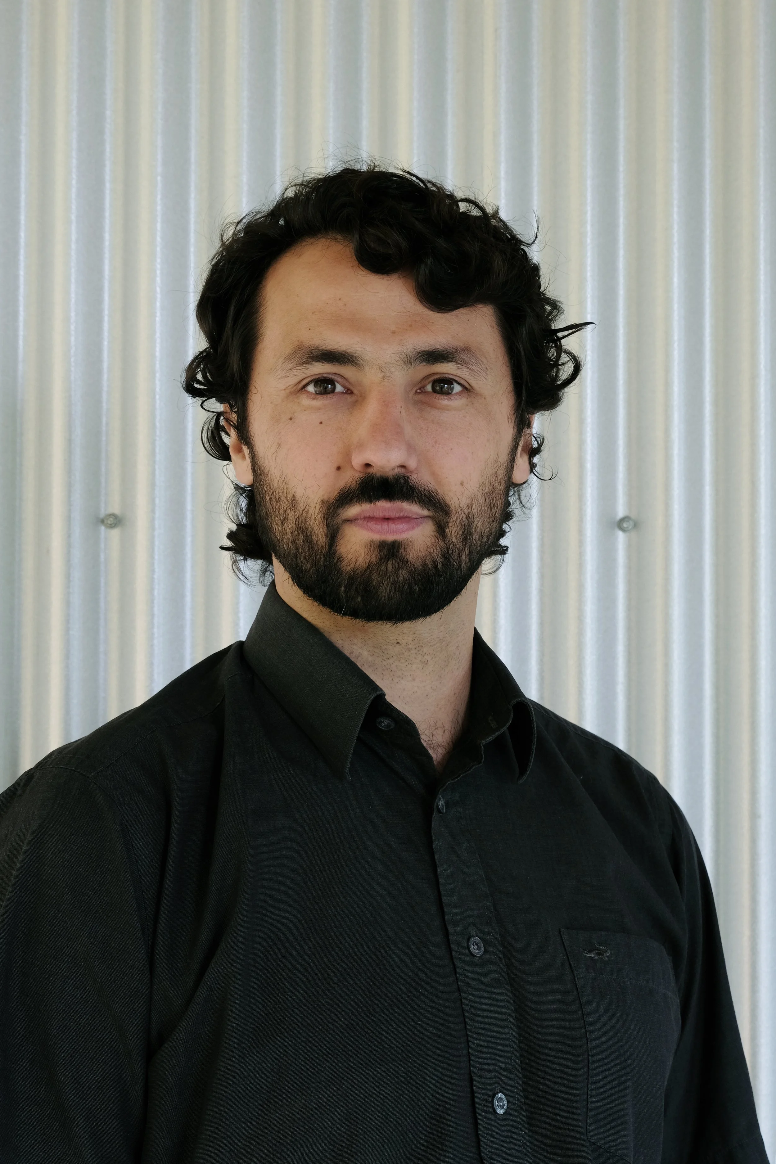Black and white portrait of a man with a beard and curly hair, wearing a suit jacket and a dress shirt, looking at the camera.