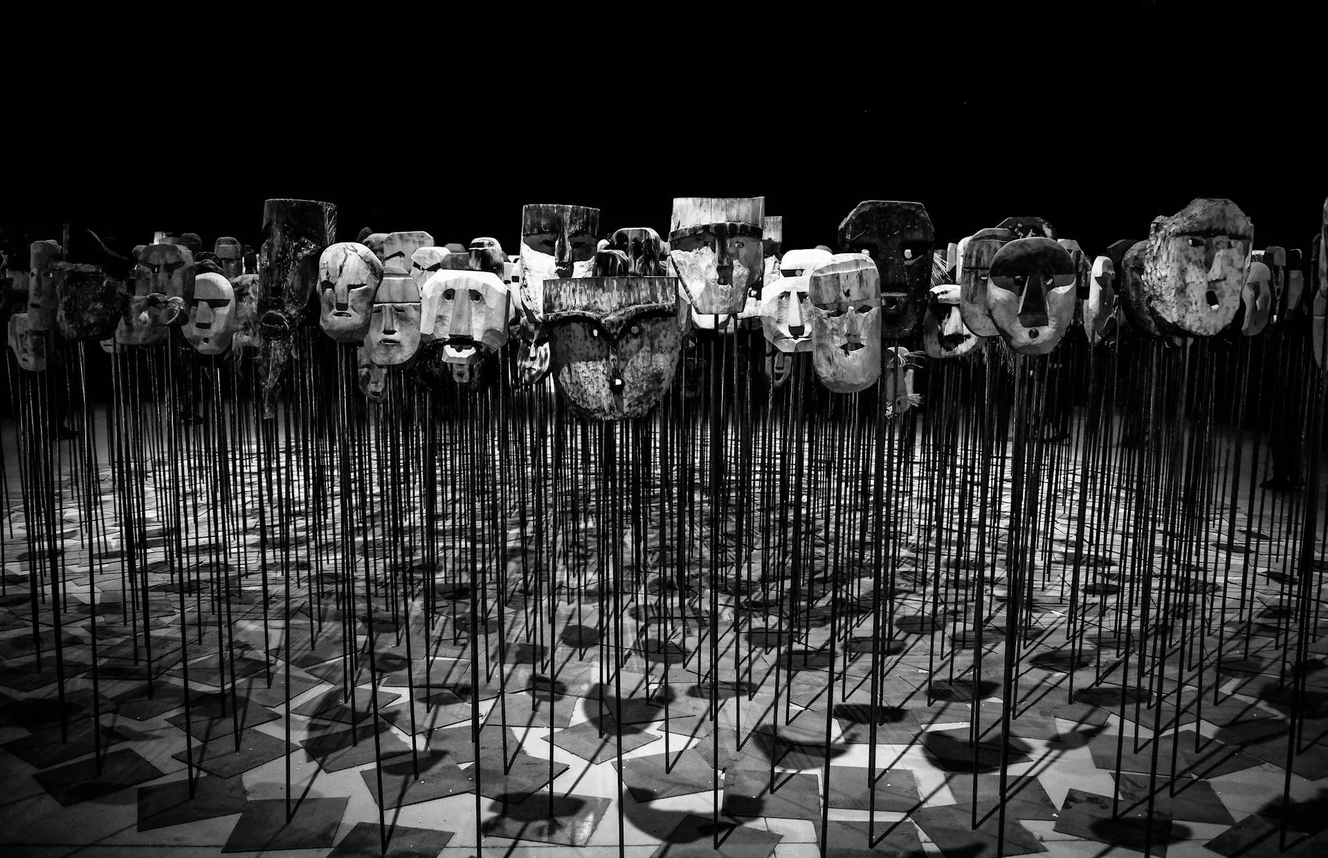 many rudimentary masks resting on stands grouped together in a starkly lit o=room