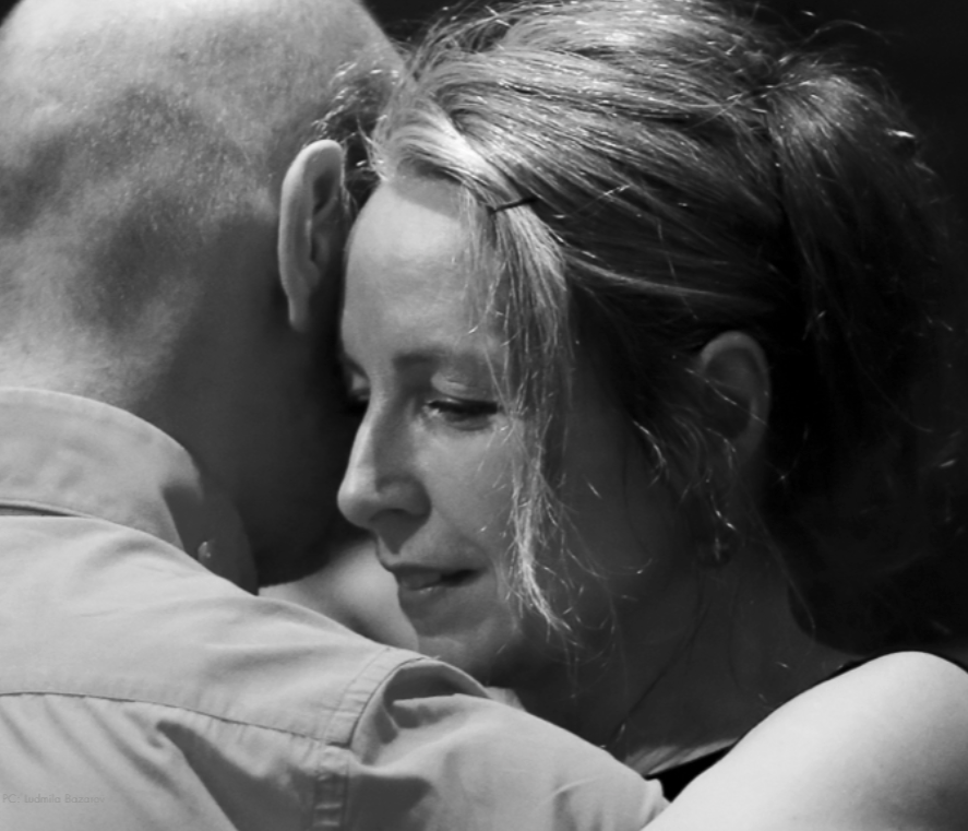 A black and white close-up of a woman and a man dancing tango, with close faces touching and eyes closed.
