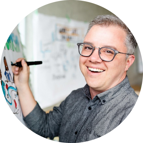 Smiling man with glasses writing on a whiteboard in a bright room.