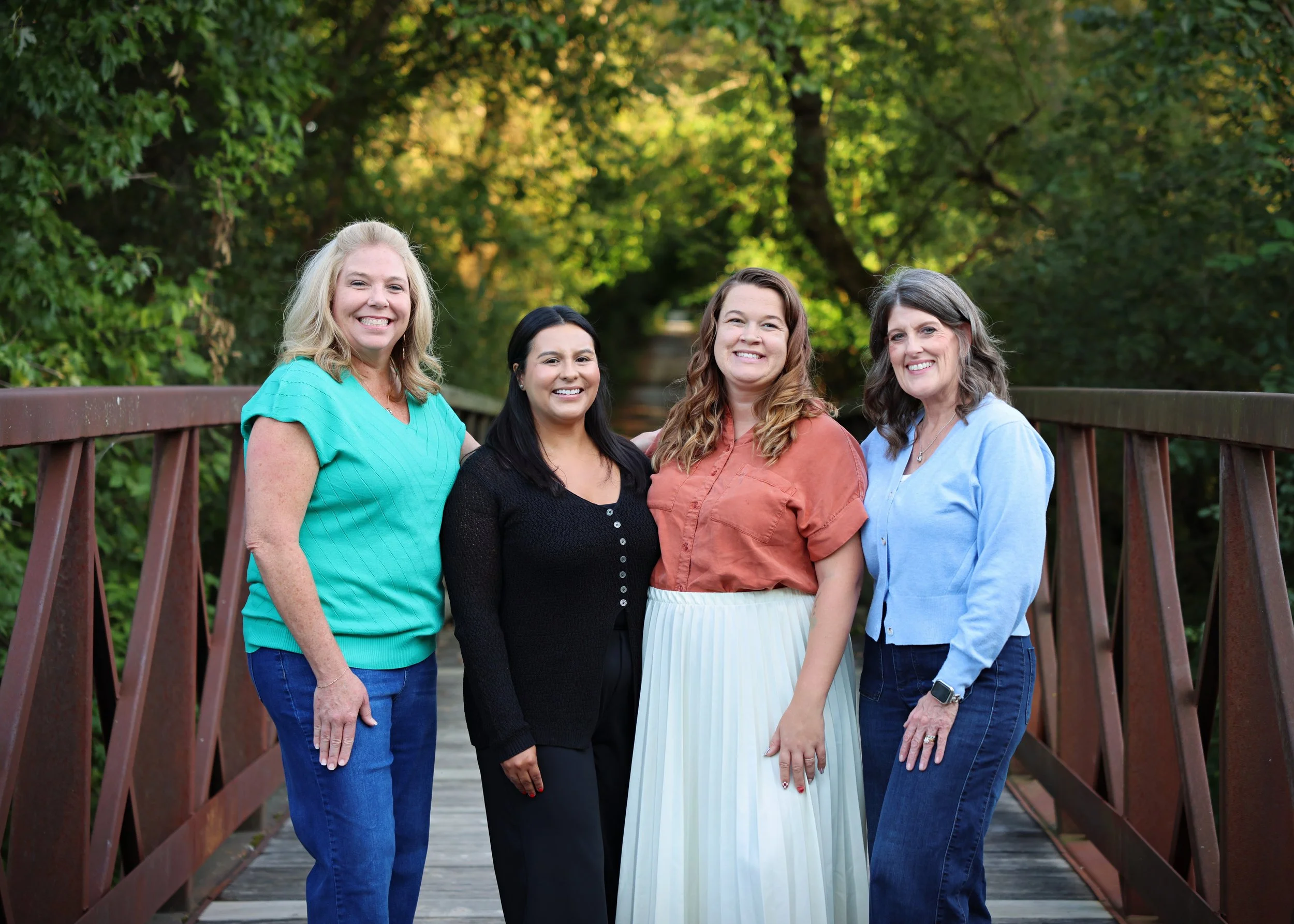 4 smiling femaie therapists standing on a bridge in the woods