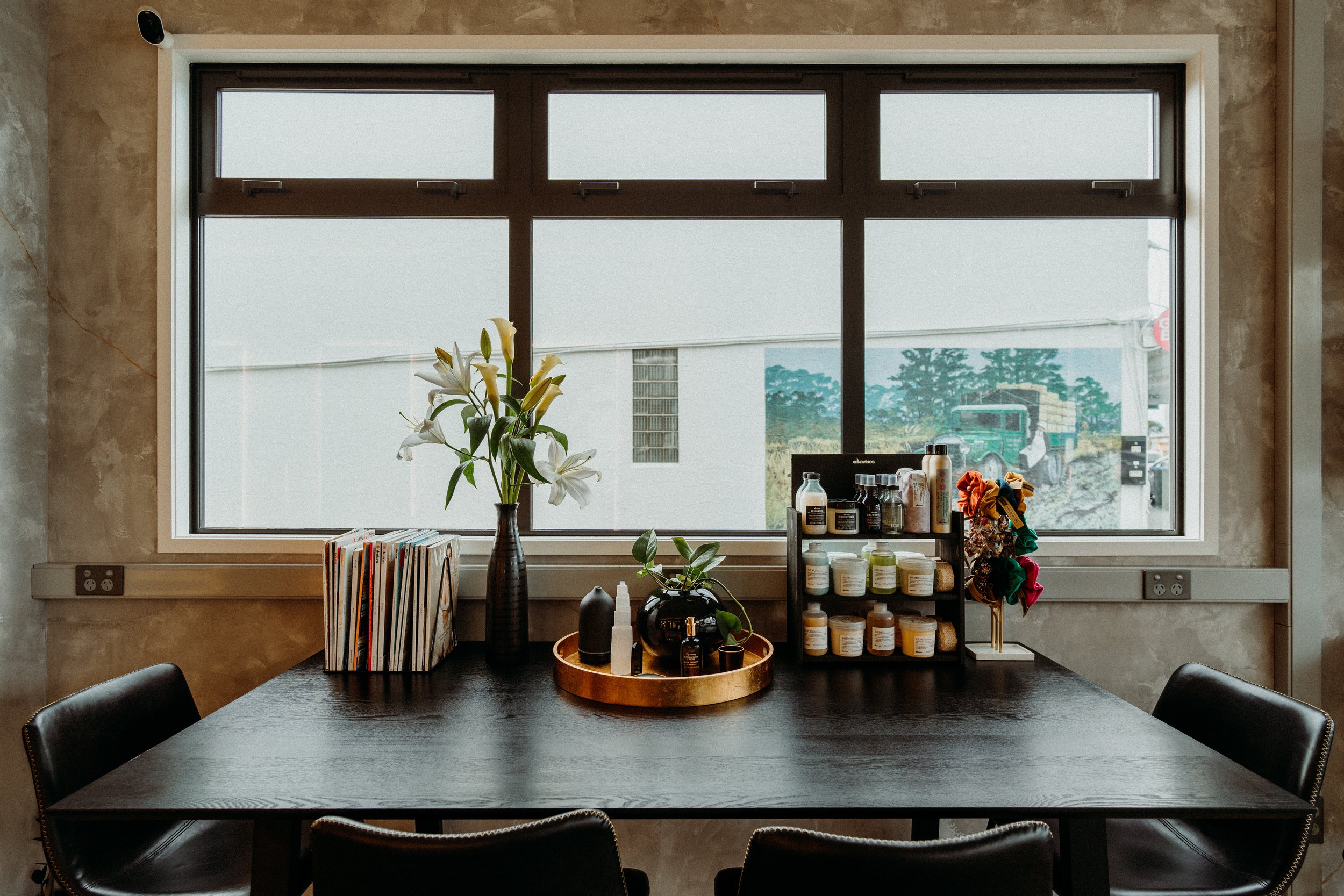modern office interior with large window, vase with flowers, magazines, and hair care products displayed on a table