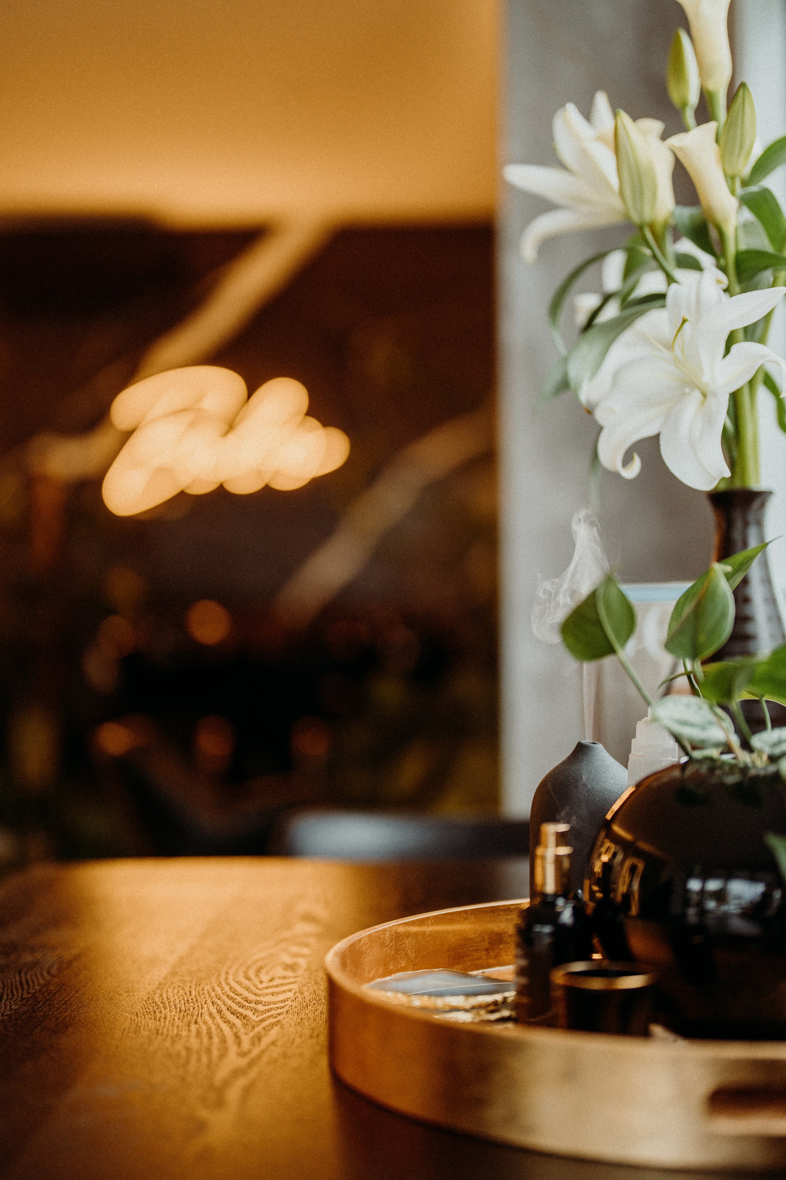 Decorative setup with white lilies, black vase, and tray on wooden table
