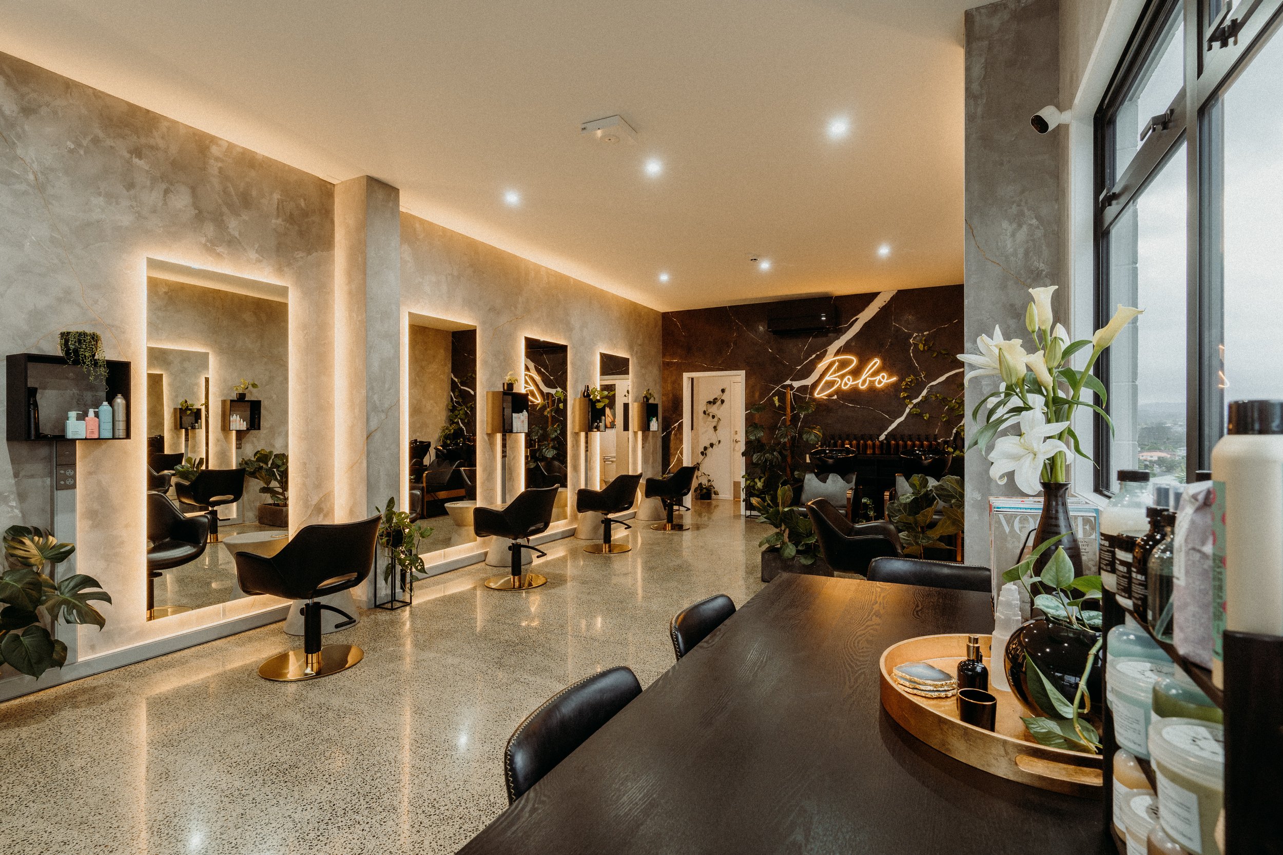 Modern hair salon interior with styling chairs, mirrors, and plants.