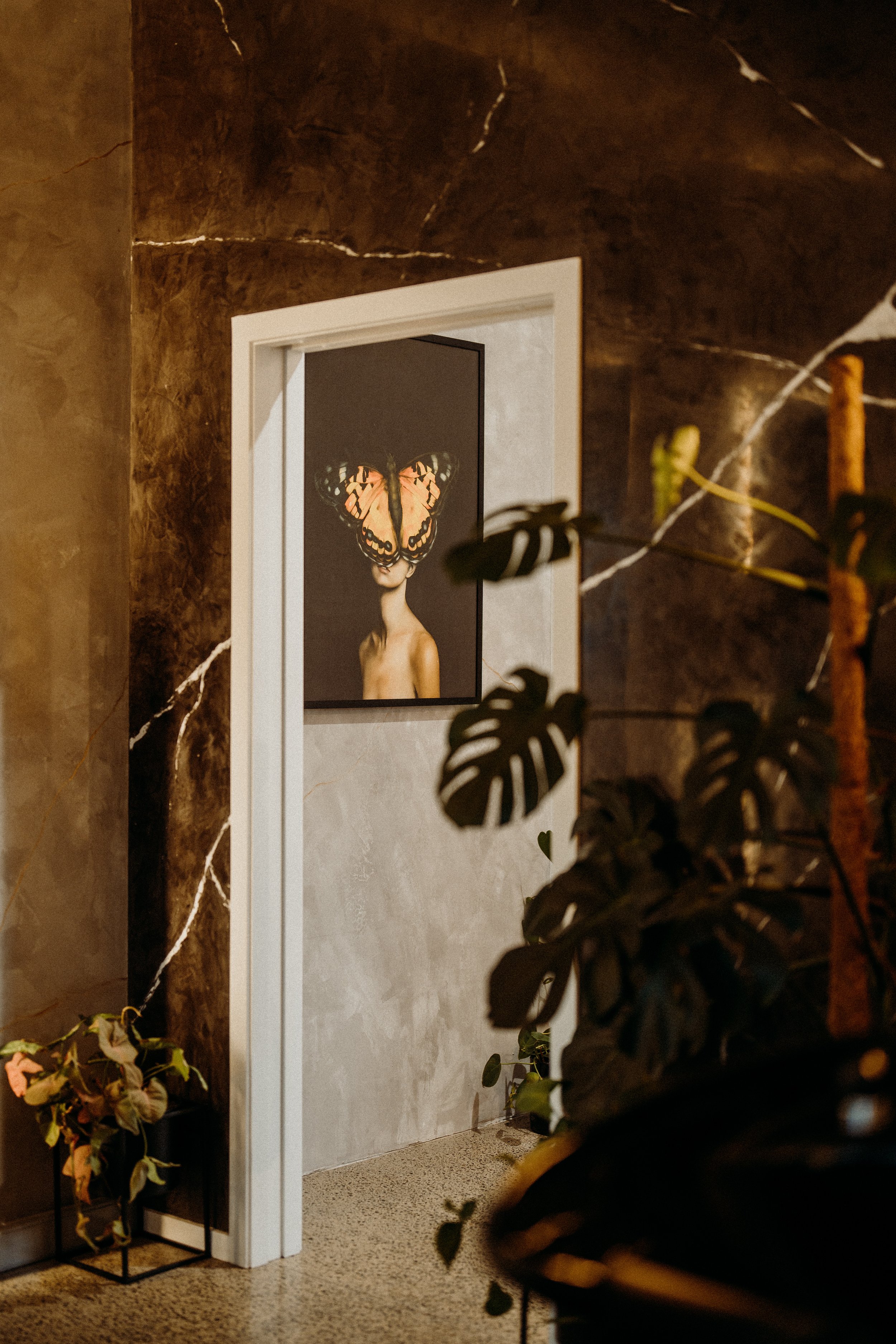 Interior hallway with a painting of a person with a butterfly on their face, surrounded by plants and textured walls.