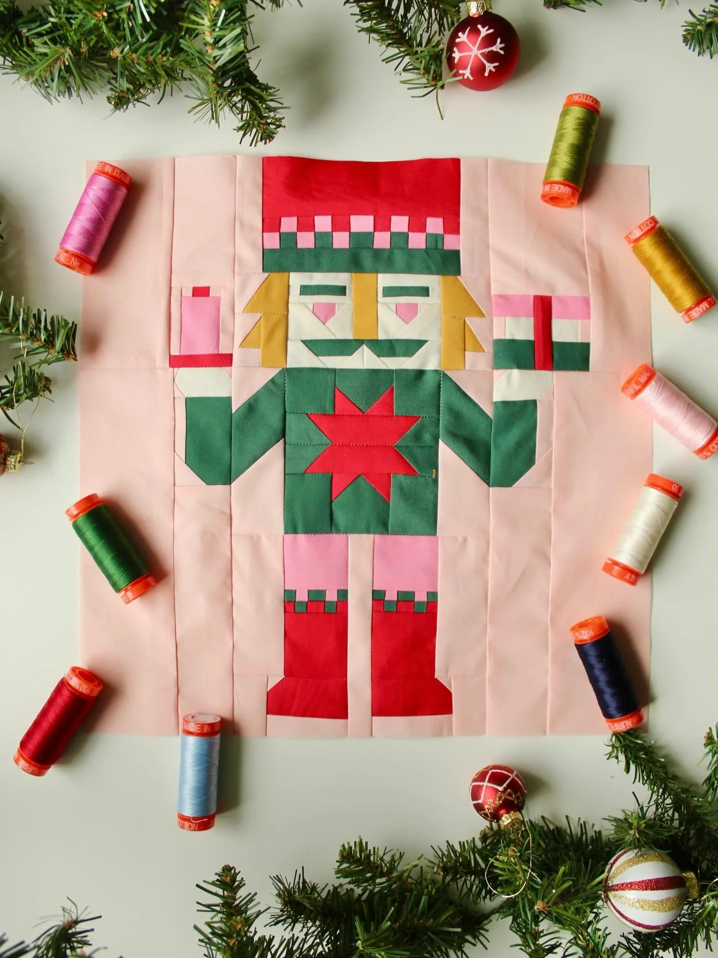 On the twelfth day of Quiltmas Katie @zahmco brings us the Quilt Nutcracker! My favorite part? This cheerful soldier is holding a stack of #agfpuresolids FQs and #aurifilthread 🥰 Perfect for all us fabric and thread lovers!

This first version is fr