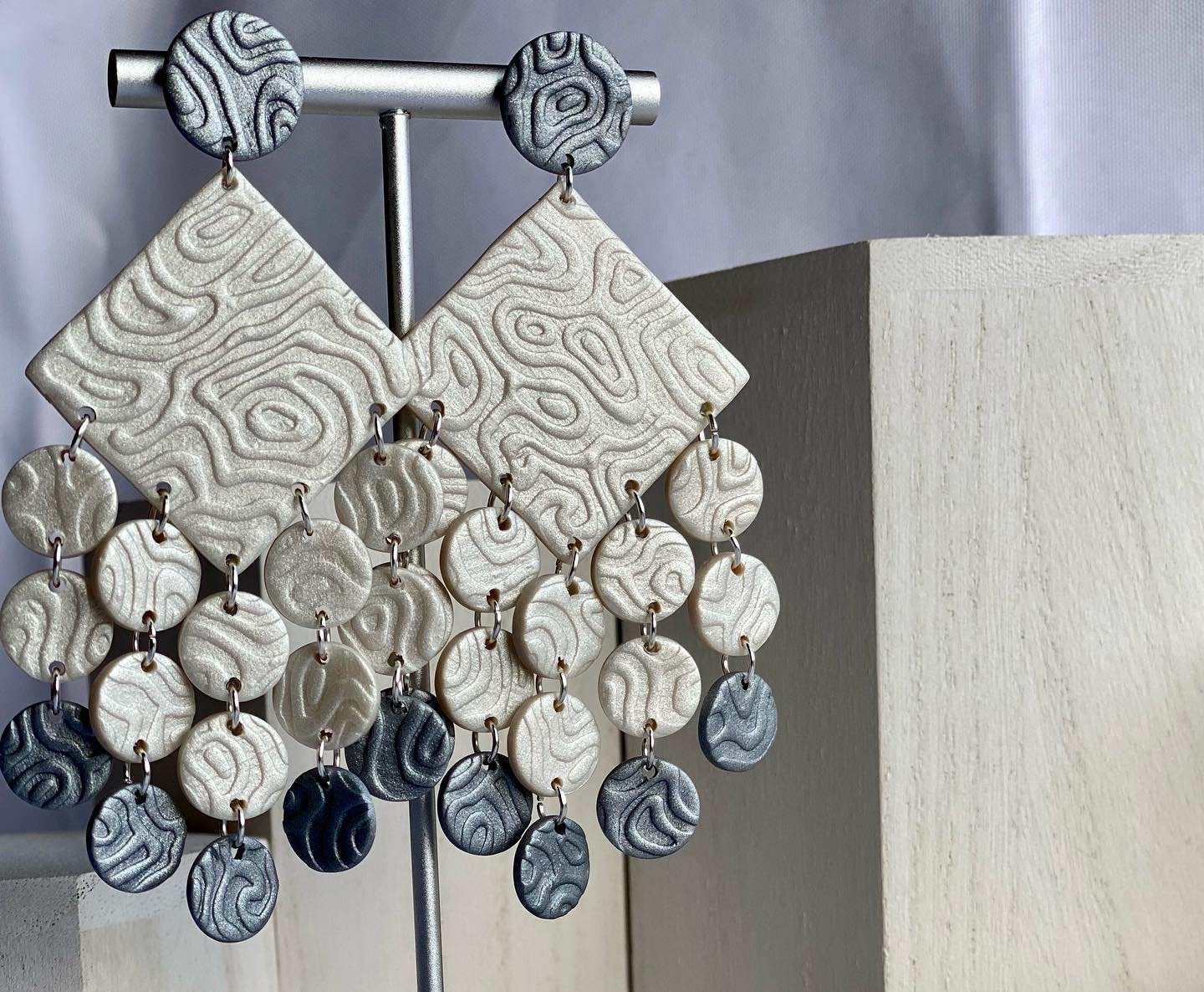 Polymer clay Textured dangling earrings with geometric and circular shapes on a display.