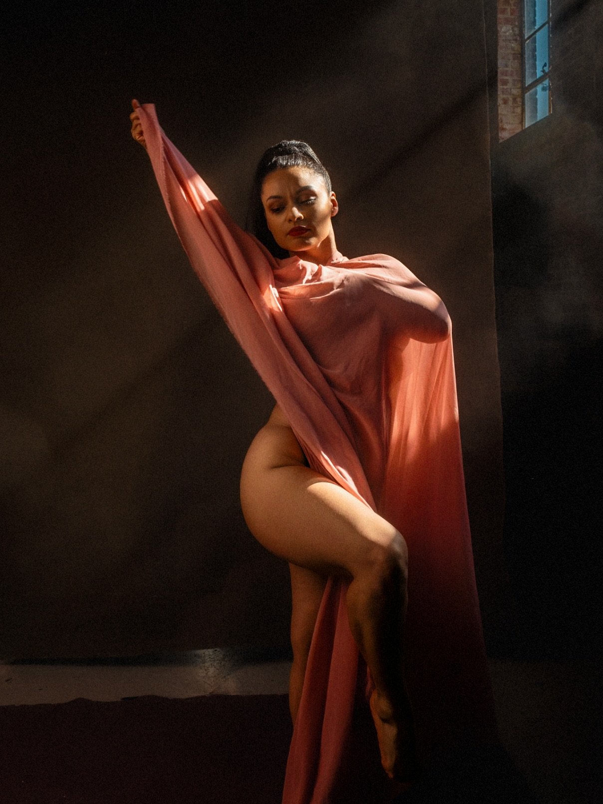 Fine art portrait of a woman wrapped in rose-colored fabric in window light