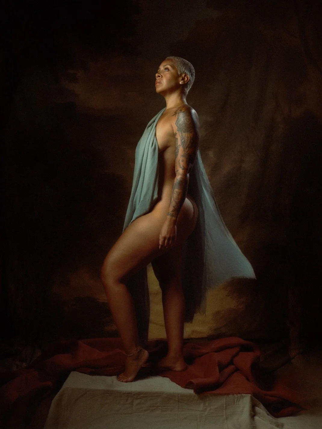 Woman in profile draped in teal cloth before a painted backdrop