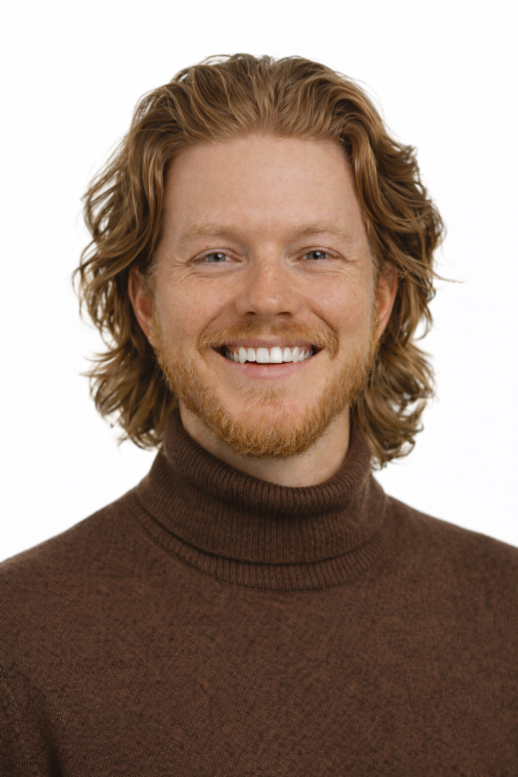 Close-up of a smiling man with red hair and beard, wearing a brown turtleneck sweater.
