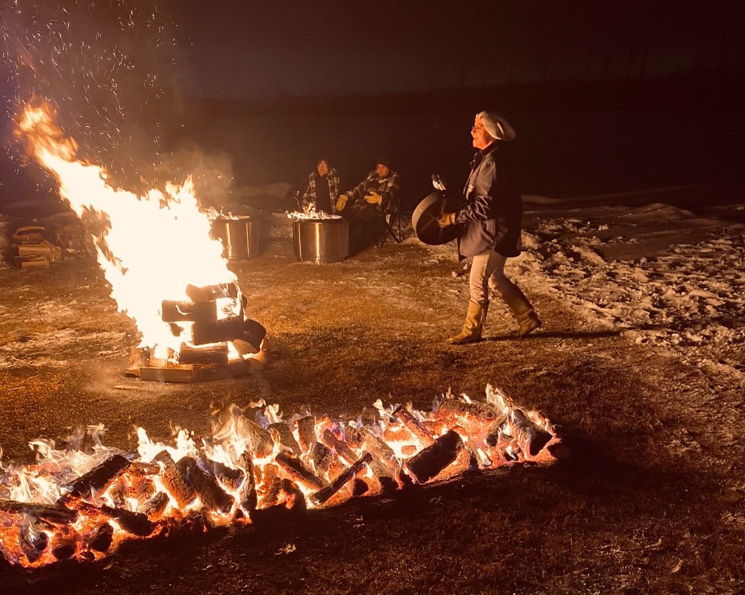 People enjoying a bonfire outdoors at night with snow on the ground.