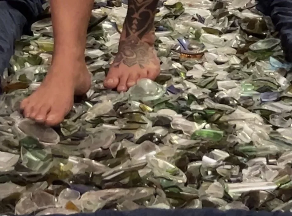 Person standing barefoot on a floor covered in shattered glass and broken glass pieces.