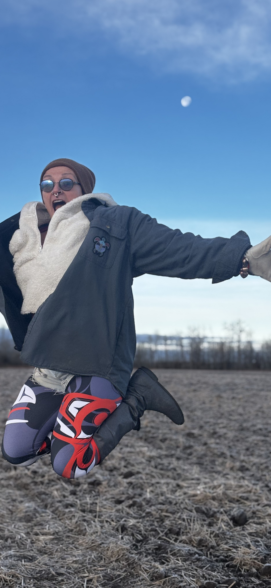 Person jumping outdoors on a dirt field during dusk or dawn under a partly cloudy sky with the moon visible.