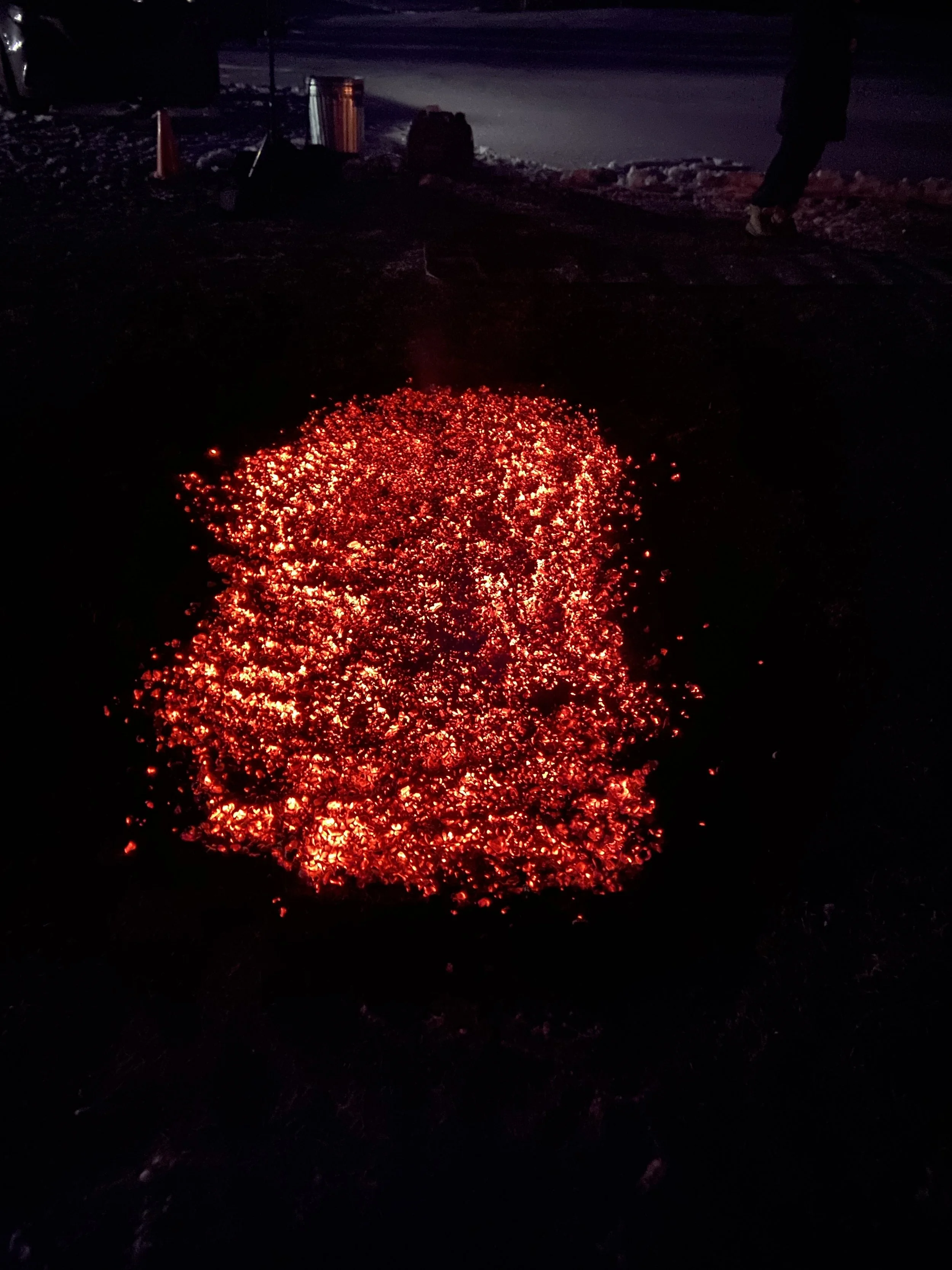 Hot, glowing embers or coals emitting red light on the ground at night.